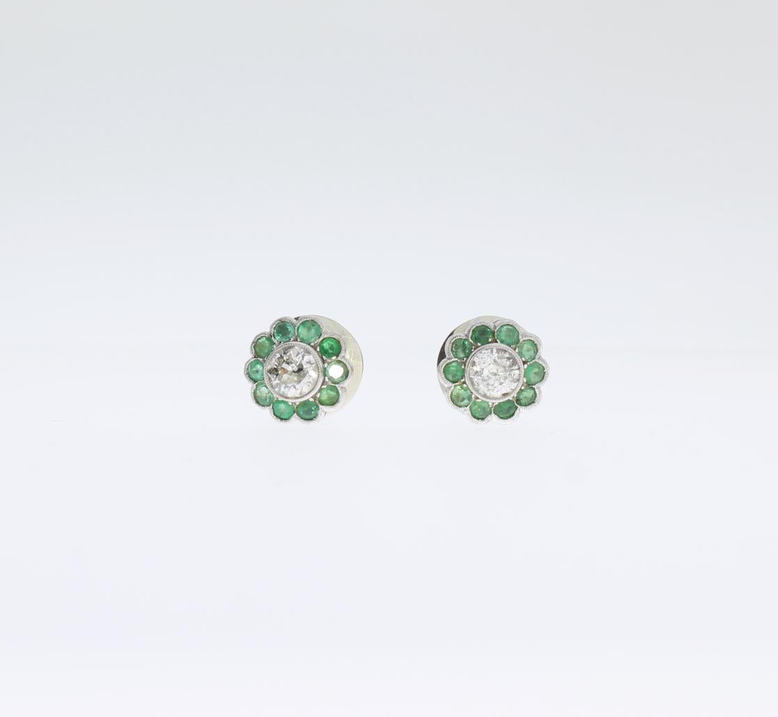 These emerald and diamond studs are designed in a floral shape, circa 1960's. With 2 brilliant-cut diamonds weighing approximately 1,20 ct. clarity: pique. Surrounded by 20 nature emeralds with a total weight of circa 1,0 ct. Mounted in white gold.