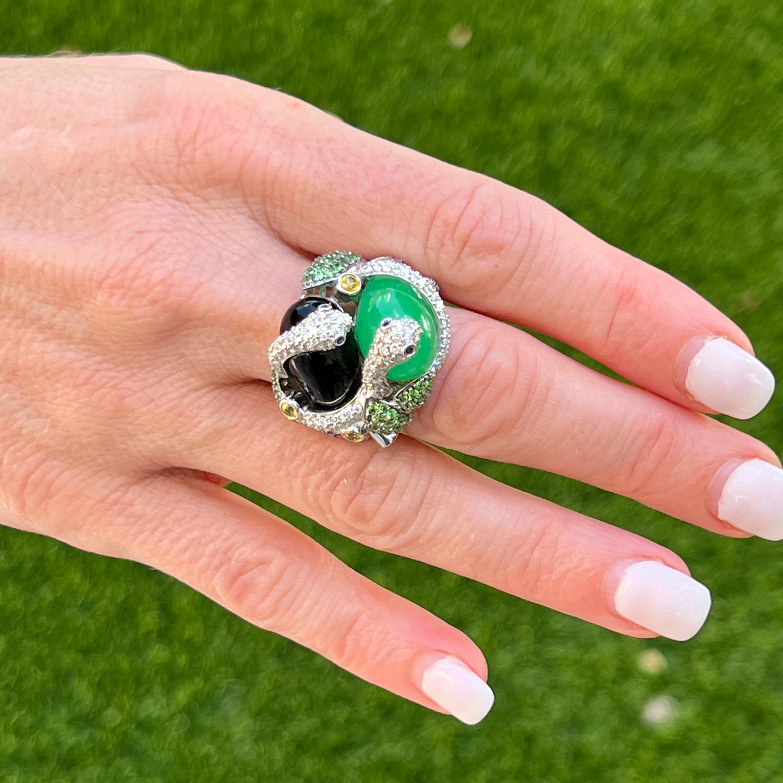 Fabulous and colorful snake ring fashioned in 18 karat white gold. The ring features cabochon emerald and onyx gemstones, diamonds, tsavorite, ruby, and yellow sapphires. The round brilliant cut diamonds weigh approximately 1.25 CTW and are graded