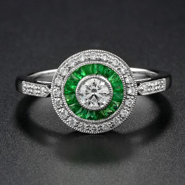 This Art-Deco engagement ring is completely spectacular! The vibrant color stone of emeralds are specialty cut to surround the excellent round brilliant cut center diamond, which is in a thin bezel with mil-grain detail. Crafted in Platinum950.