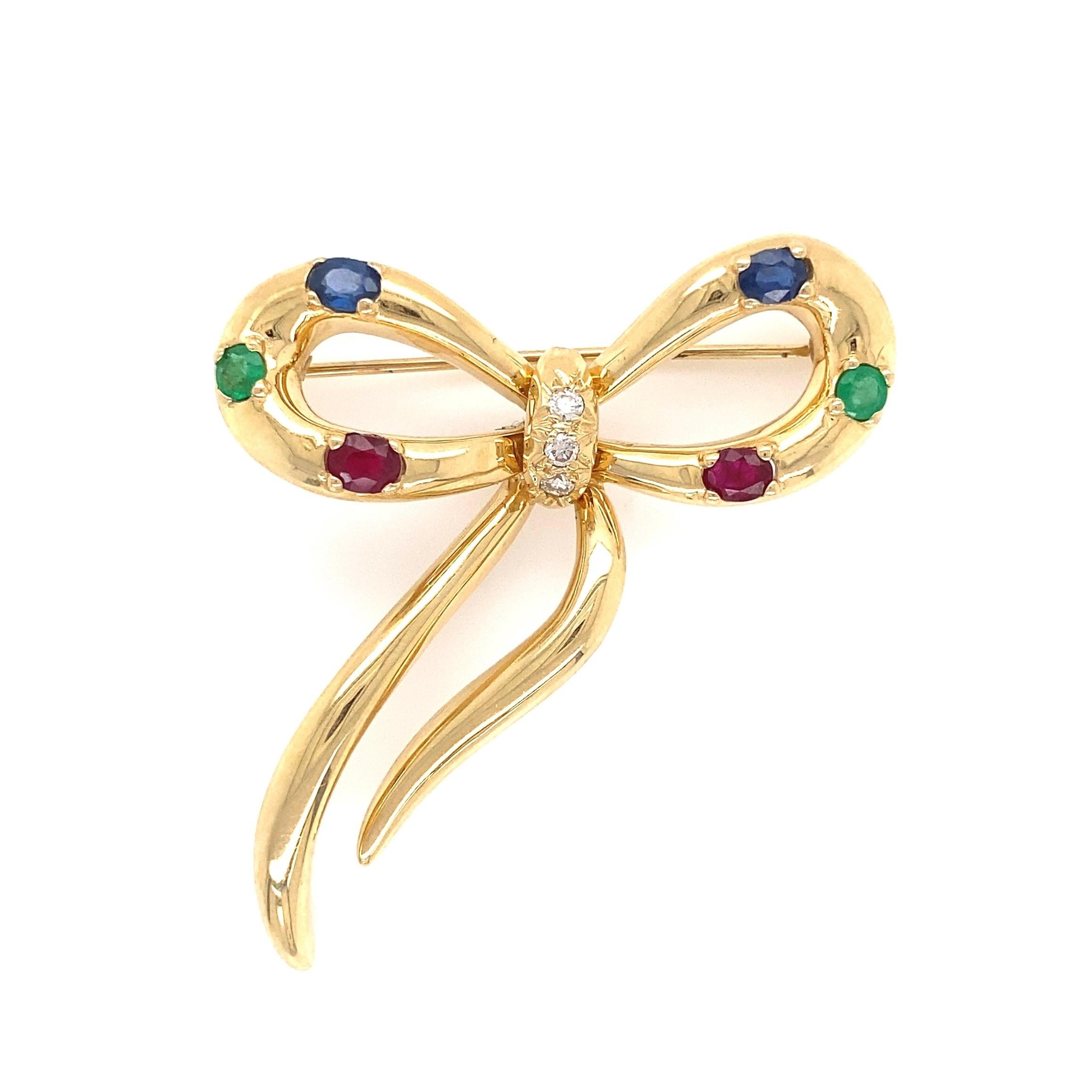 Beautiful Ribbon Bow Multi-Gem Gold Brooch. Hand crafted in 14K Yellow Gold and Hand set with 3 Diamonds approx. 0.08tcw in center and enhanced around the bow with 2 oval Rubies approx. 0.50tcw, 2 round Emeralds approx. 0.28tcw and 2 oval Sapphires
