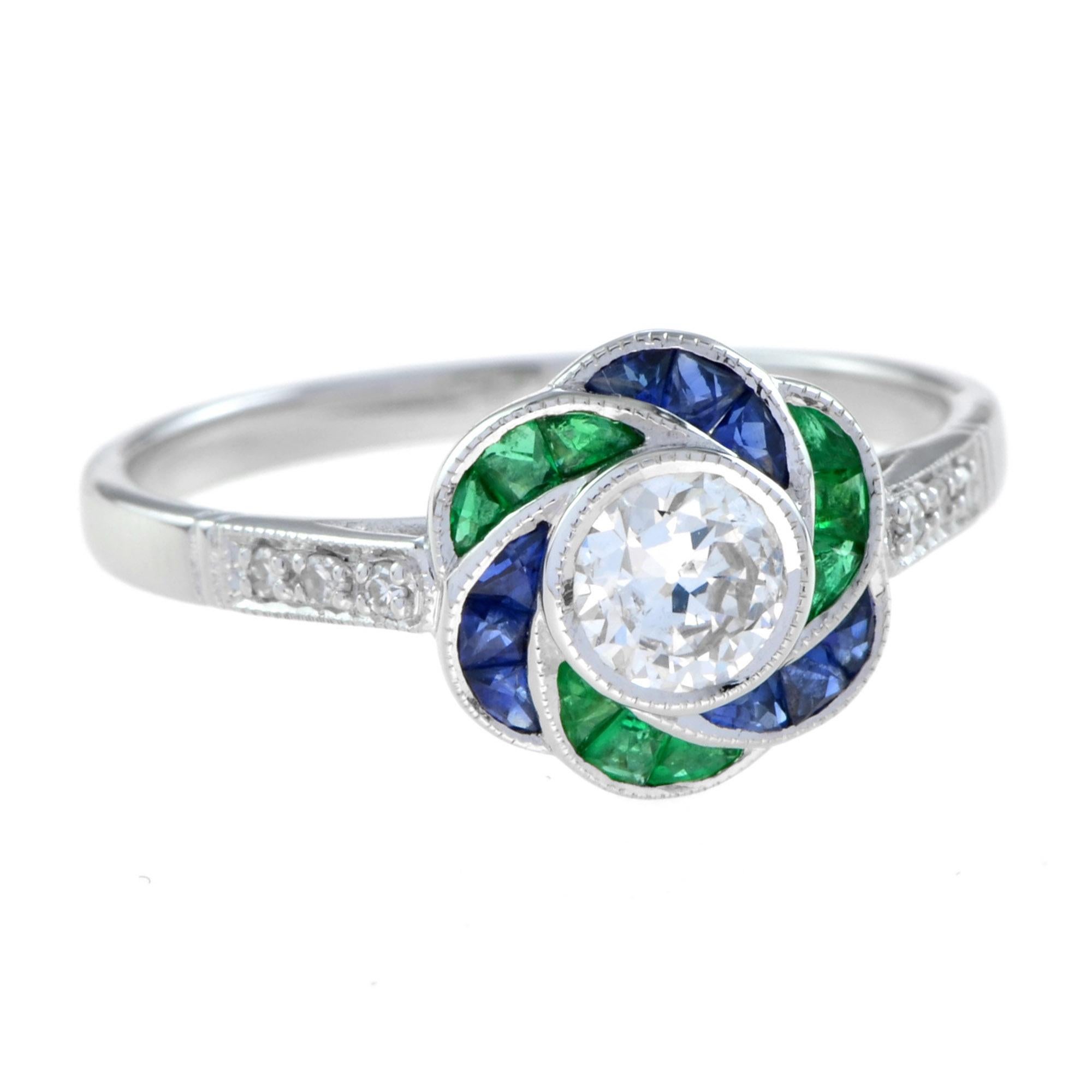 Arte y sofisticación se unen en un anillo flor con diamante, esmeralda y zafiro de la época Art Déco. El anillo presenta un diamante central de forma redonda en un engaste de bisel rodeado de zafiro azul de talla francesa y esmeralda para sus