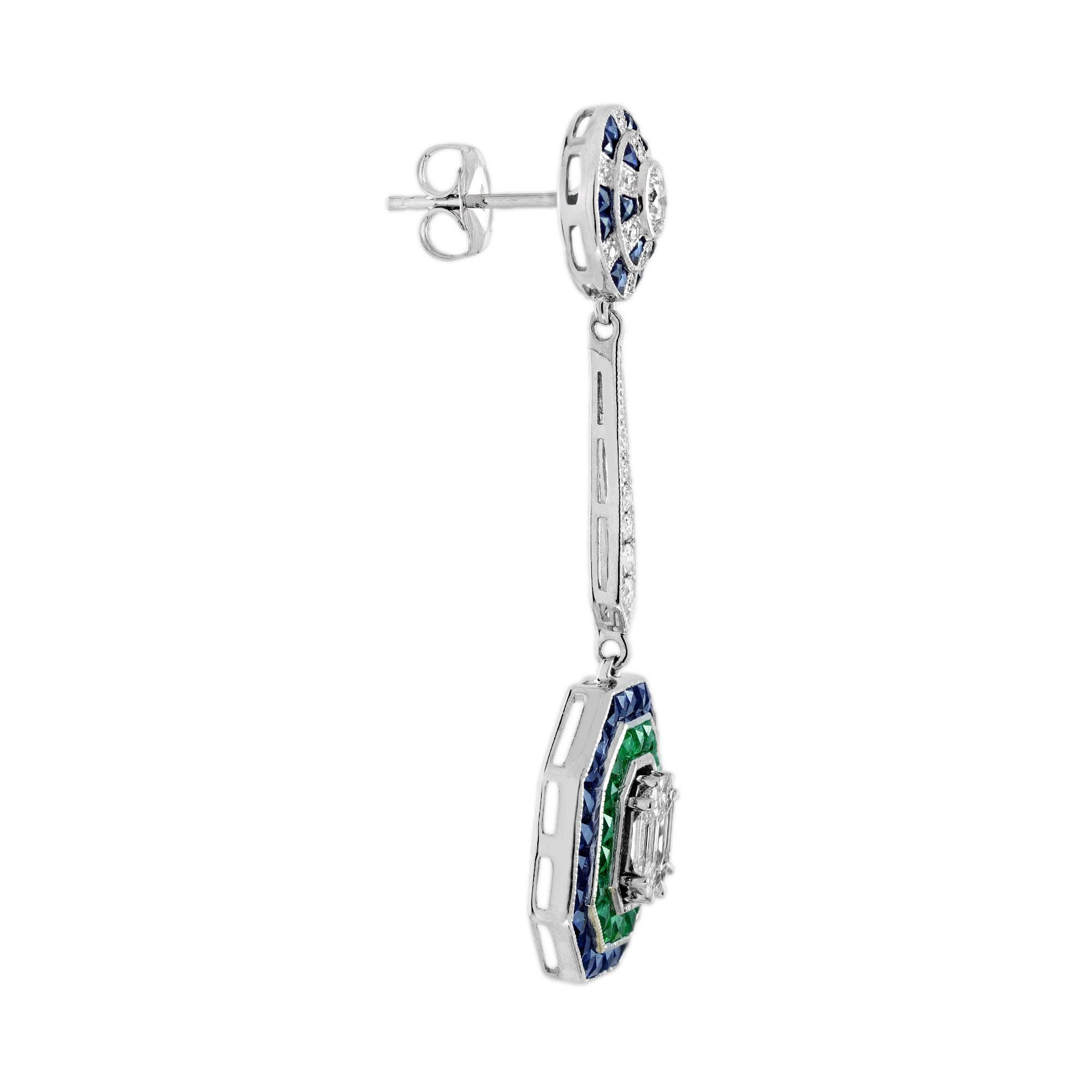 Ces boucles d'oreilles pendantes en diamant, émeraude et saphir de style Art déco présentent un design époustouflant qui commence par une forme ronde, alternant diamants et saphirs dans un motif accrocheur au niveau de la partie du lobe. Les boucles