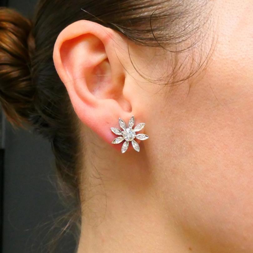 Un paio di orecchini con diamanti floreali in oro 14k. 
Ogni orecchino presenta un diamante rotondo centrale con taglio a brillante circondato da un'aureola di elementi a forma di petalo. Ogni petalo è ornato da un singolo diamante tagliato. Questo