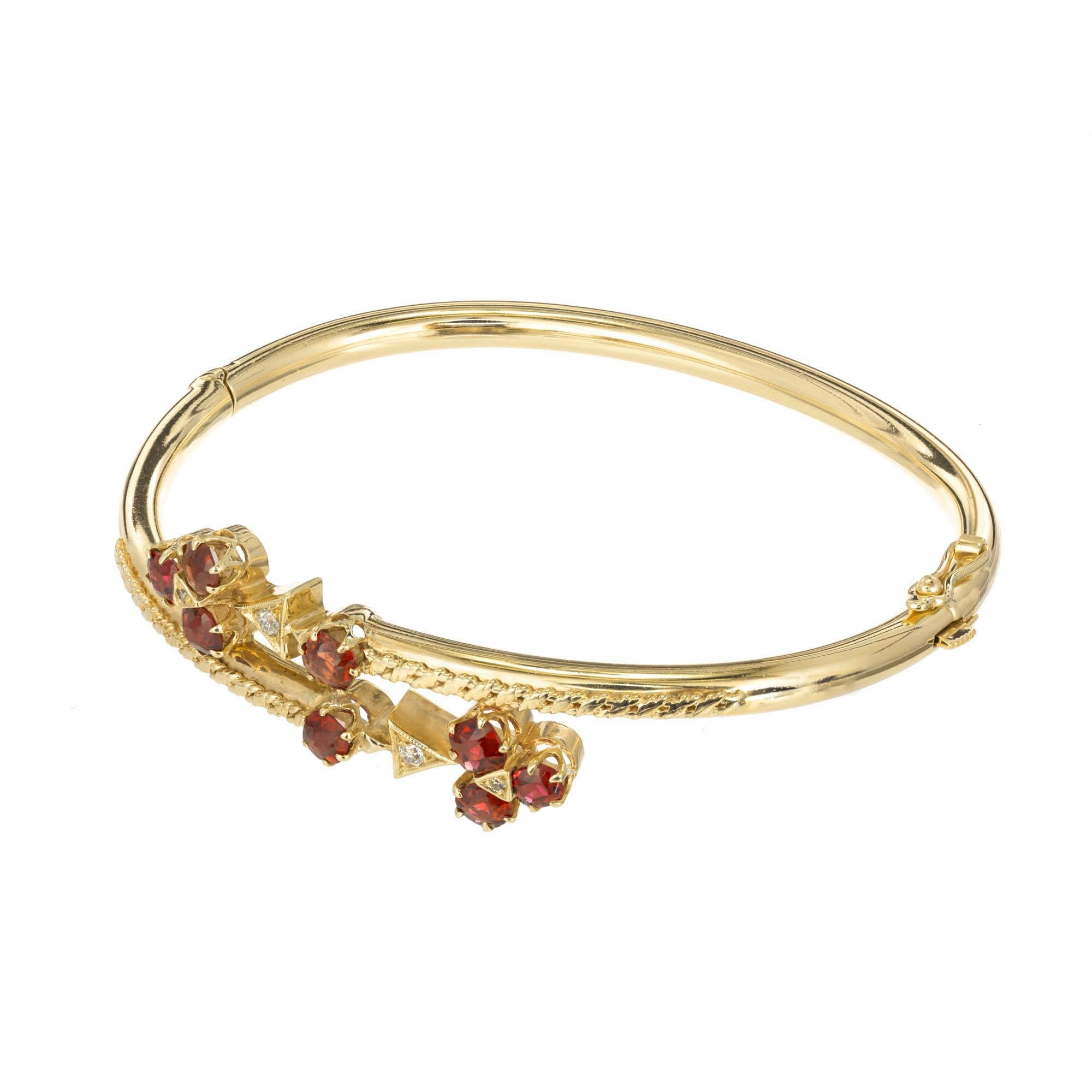 14k Yellow gold diamond and garnet bypass bangle. Three round garnets prong set with a diamond in the center attached to a triangular setting with a round diamond makes a clover like design attached to an additional garnet.
 
8 old European cut