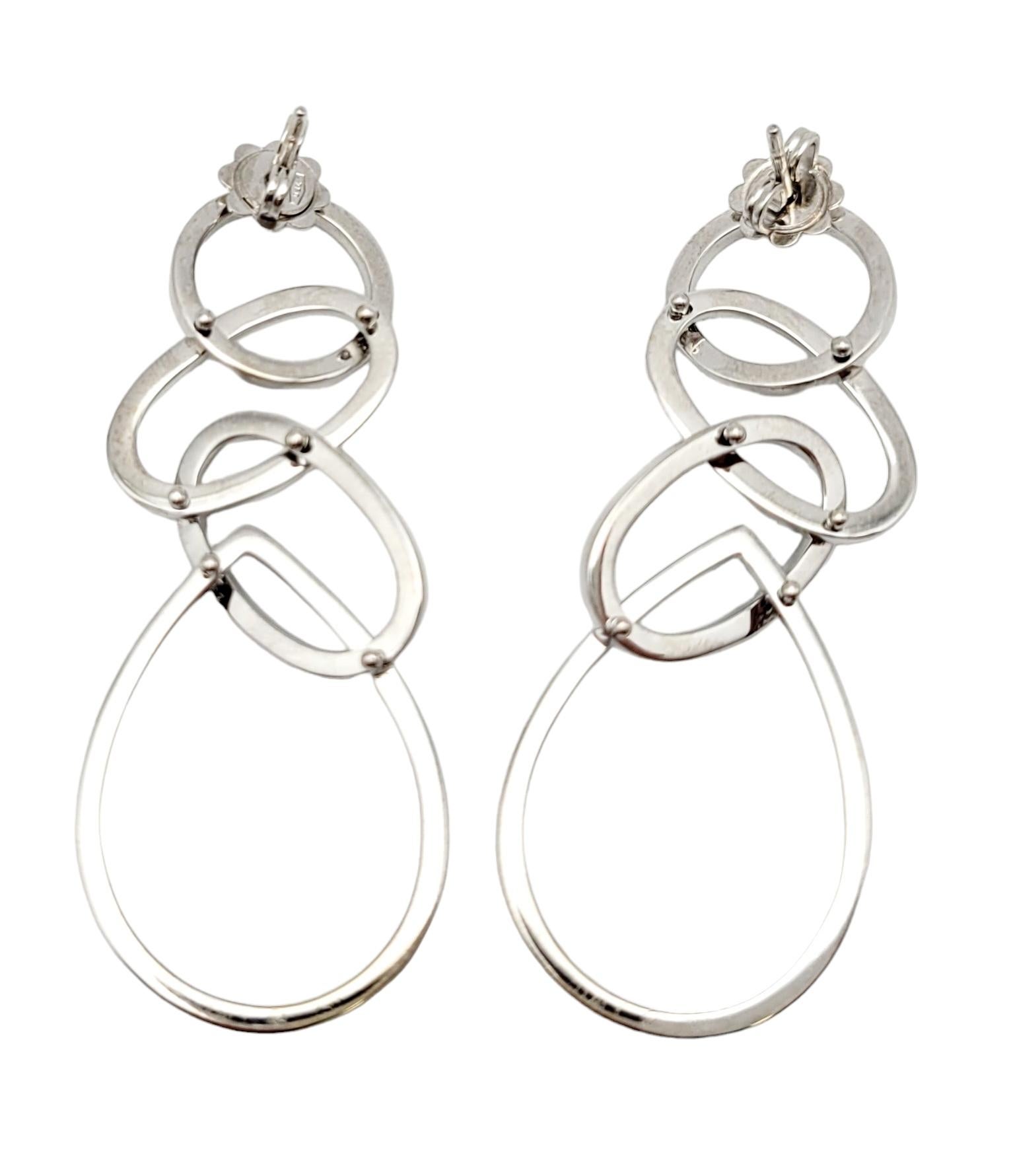 Emanating sophistication and modern elegance, this pair of diamond and gold earrings is a true work of art. Expertly fashioned from gleaming 18 karat white gold, the earrings showcase a distinctive dangle design that seamlessly blends interlocking