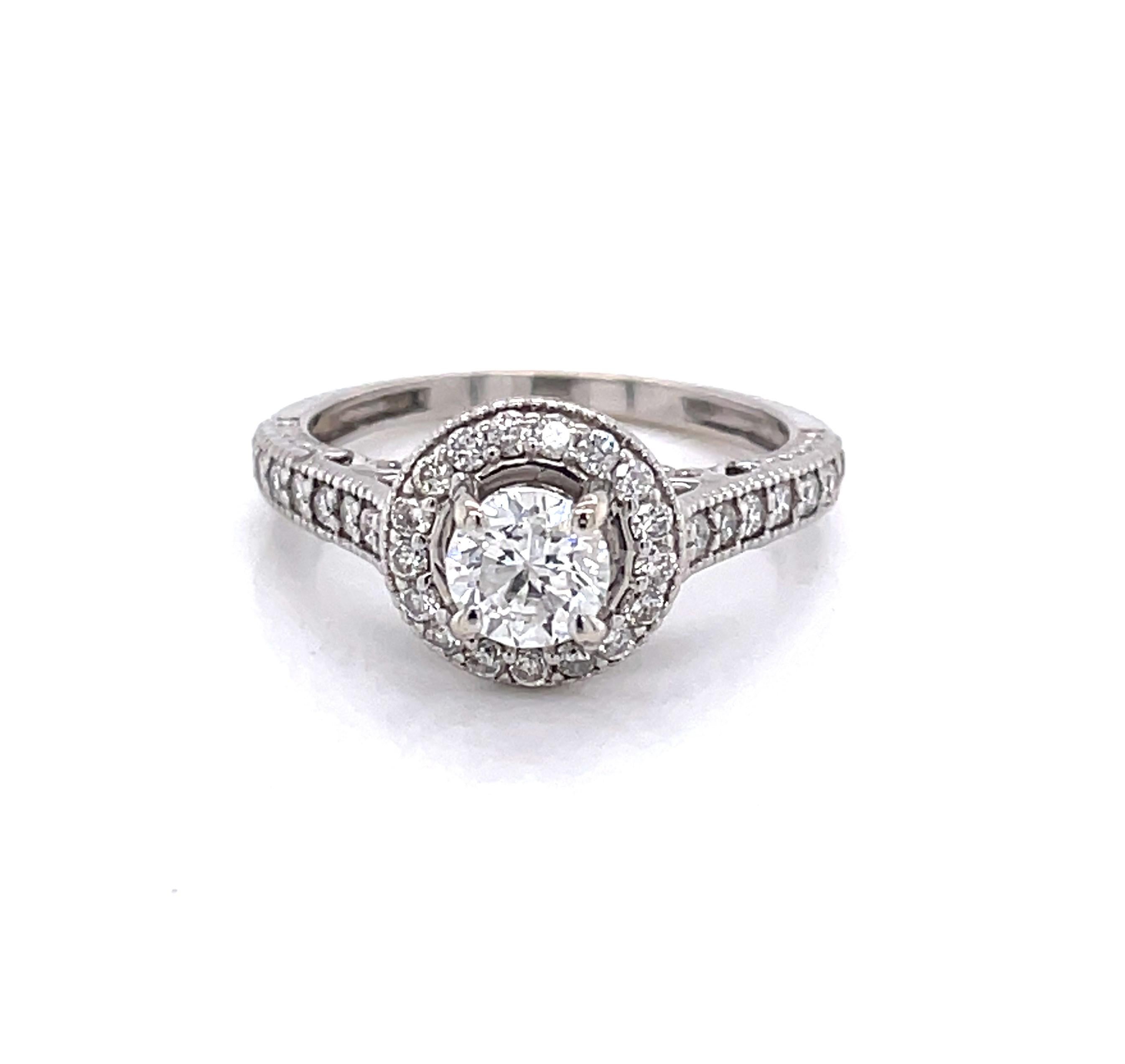 A  .53 carat H/VS round facet cut center diamond encircled with a diamond encrusted halo is the feature of this elegant engagement ring in fourteen karat 14k white gold. Fourteen sparkling side stones further illuminate the band. Total diamond carat