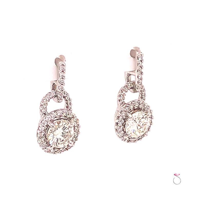Superbes boucles d'oreilles pendantes avec halo de diamants en or blanc 18 carats. Ces magnifiques boucles d'oreilles sont ornées de deux diamants ronds de taille brillante au centre, chacun mesurant approximativement 5,80 mm x 5,80 mm x 3,45 mm