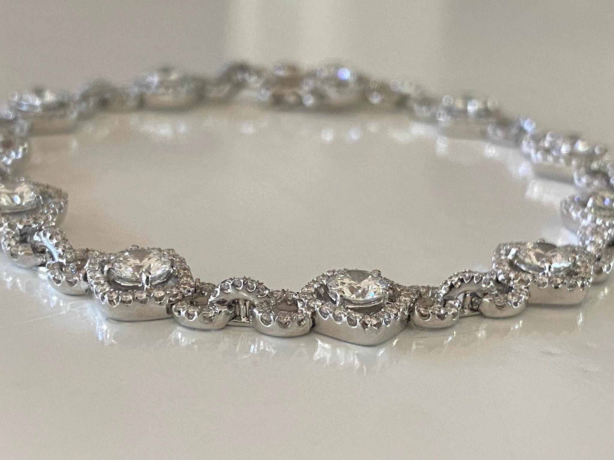 This dazzling diamond bracelet features eleven round brilliant-cut diamond center stones each measuring 0.27 carats, F color, SI1 clarity, surrounded by a halo of round diamonds connected by circular diamond links and fashioned from 18kt white gold.