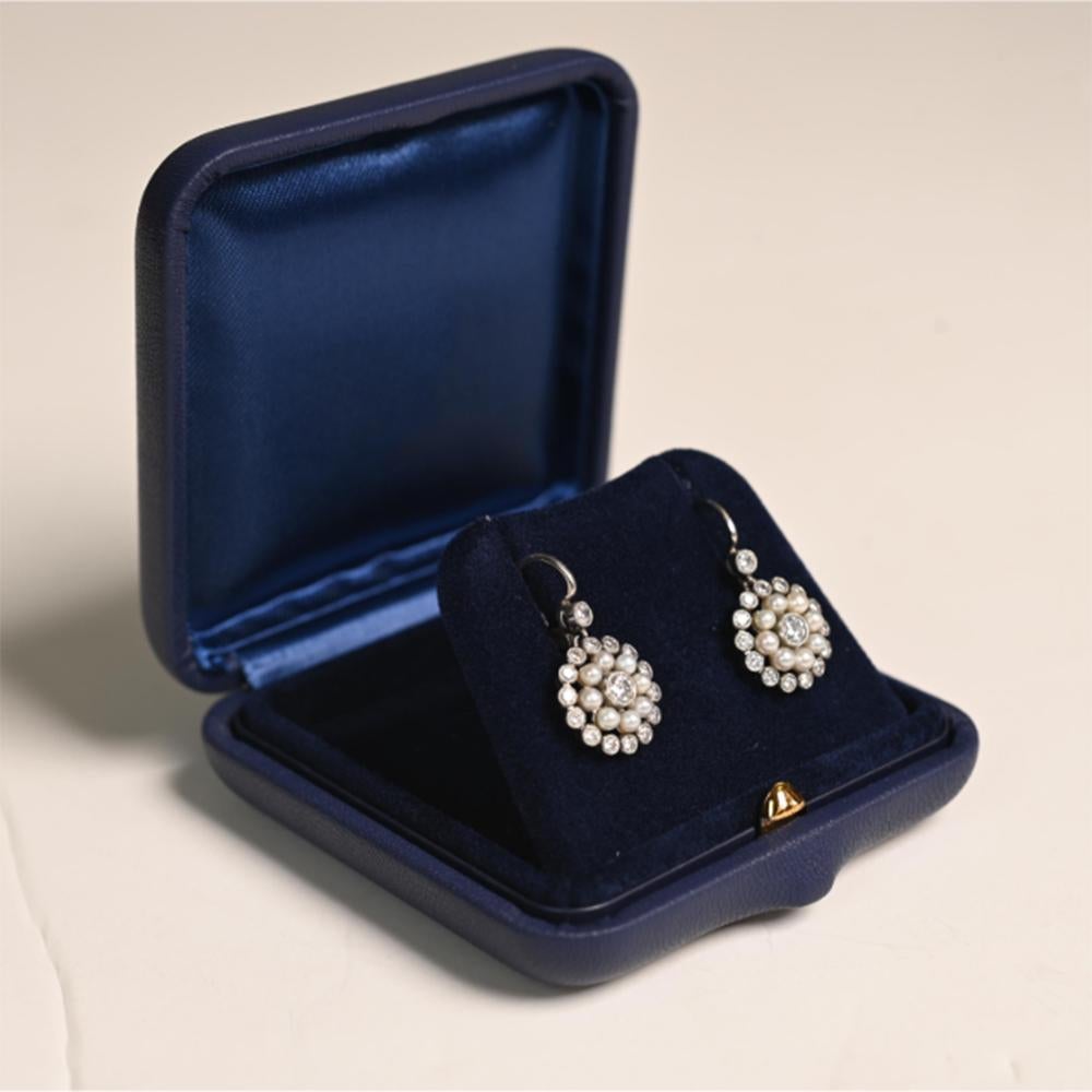 Cette exquise paire de boucles d'oreilles de style Elegardien met en valeur l'élégance intemporelle de l'artisanat des perles et des diamants. Les boucles d'oreilles présentent chacune un diamant central pesant environ 0,08 carat, entouré d'un