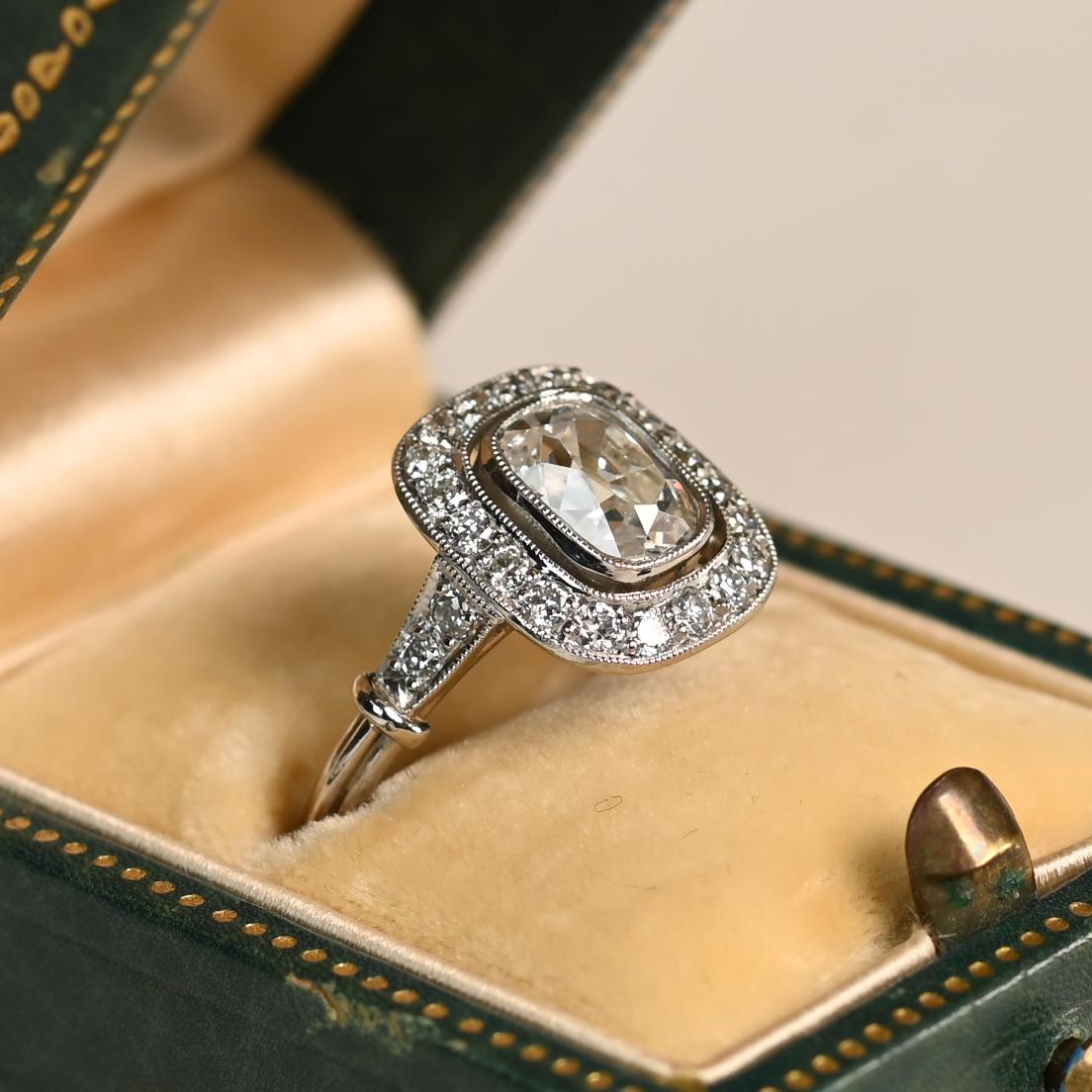 Cette exquise bague de fiançailles de style vintage Diamond Halo met en valeur un superbe diamant antique de taille coussin, certifié par le GIA à environ 1,20 carats, d'une couleur G et d'une pureté SI1. Le diamant central rayonne d'une élégance