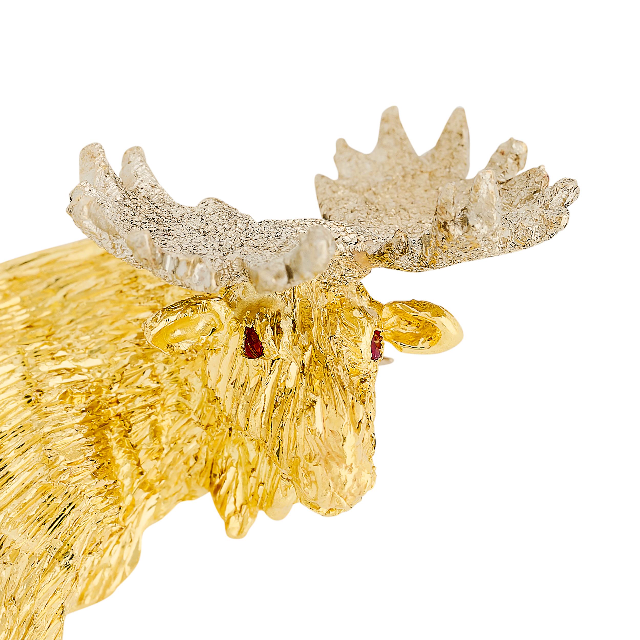 Diese auffällige Elch-Anstecknadel besteht aus strukturiertem Gelbgold für den Körper, mit einem großen, dramatisch strukturierten Geweih aus Weißgold oder Platin, Rubinaugen und einem einzelnen, markanten Diamanten, der einen der Füße betont.
Es