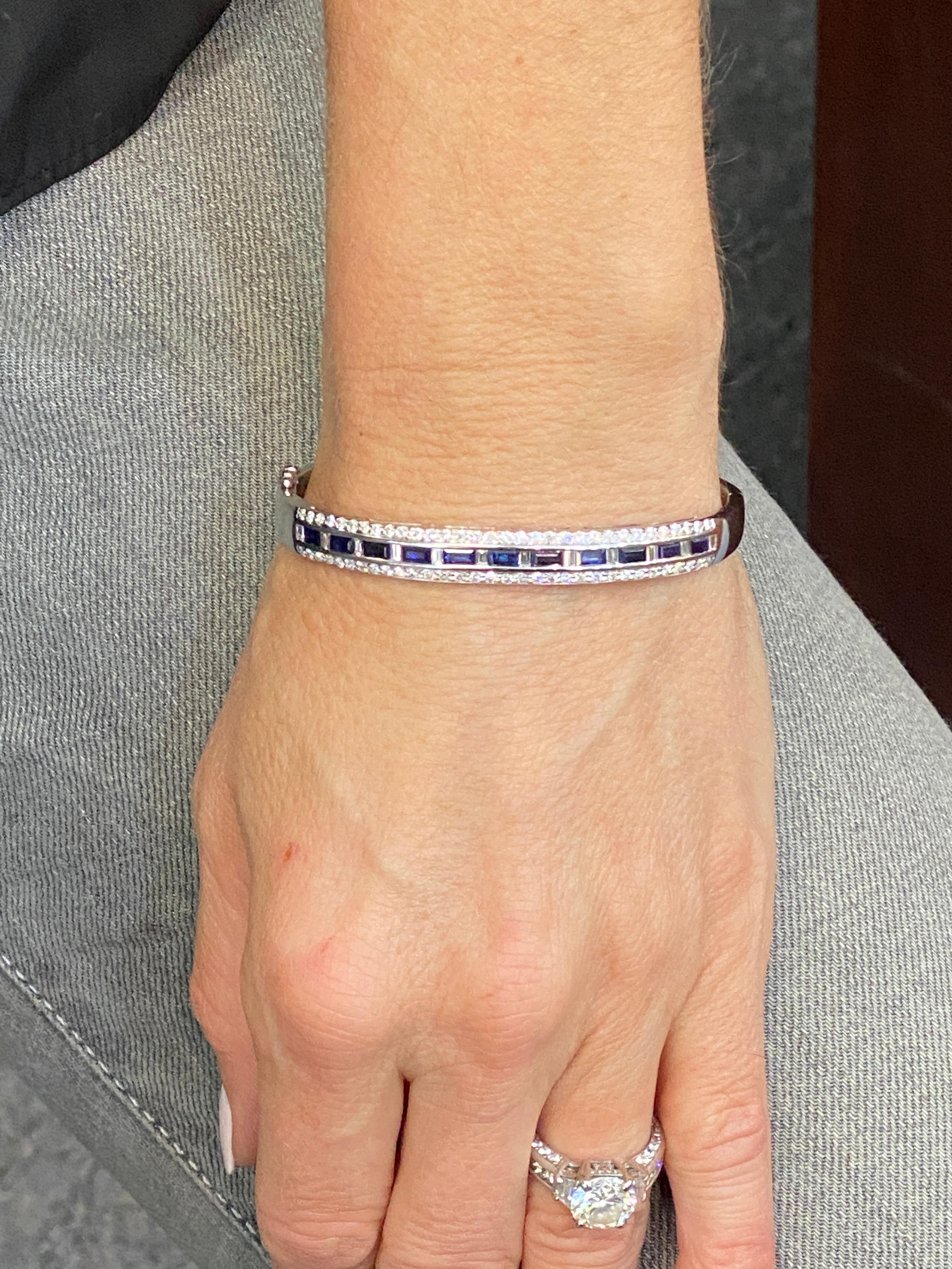 Diamond and natural blue sapphire bangle bracelet crafted in 18 karat white gold. The bangle features 76 round brilliant and baguette cut diamonds weighing approximately 1.12 carat total weight and 11 natural blue sapphires weighing approximately