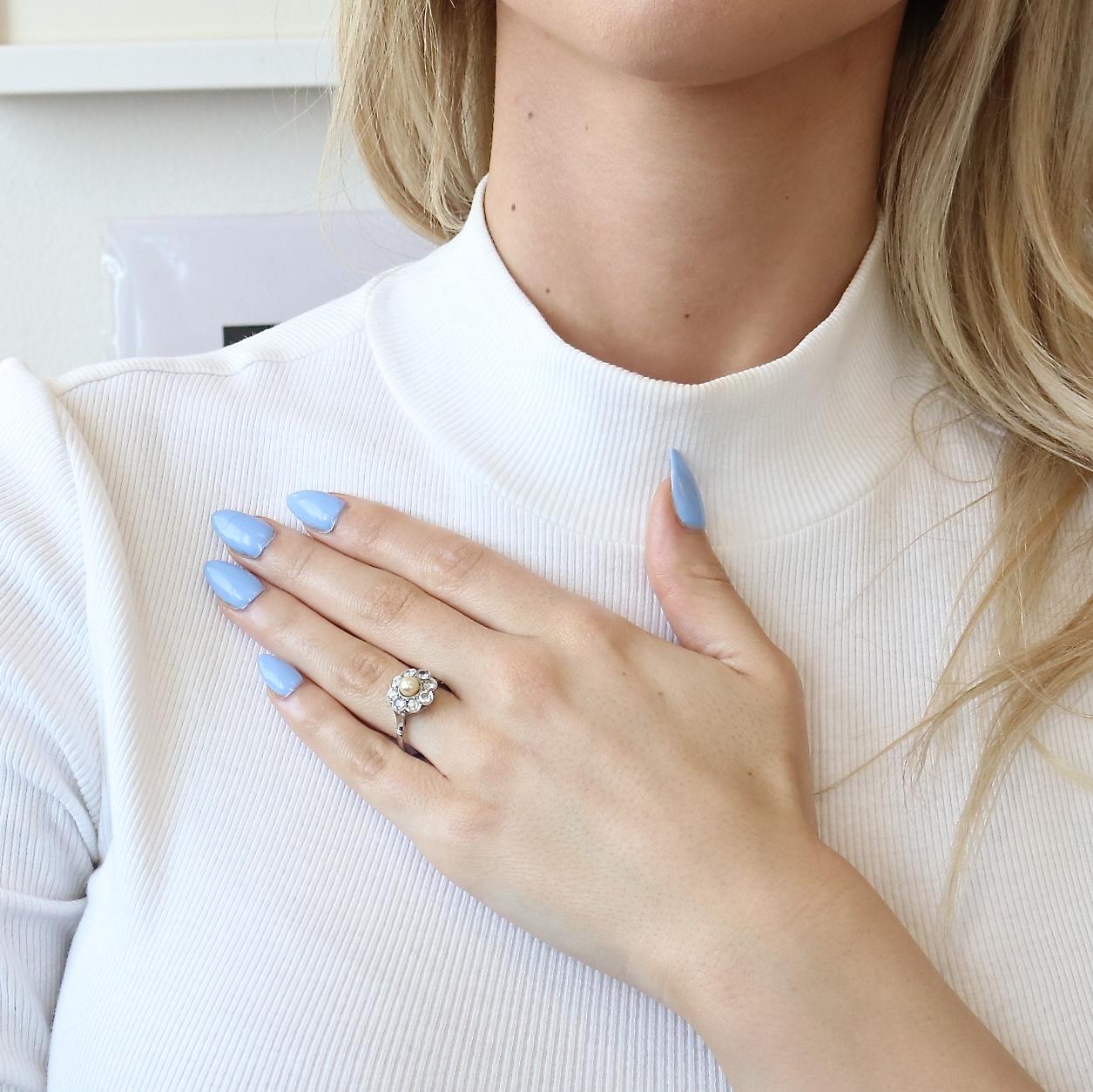 This Edwardian inspired diamond pearl cluster ring represents the refined aesthetic of the era. Set in platinum, the floral cluster that surrounds the natural pearl contains 8 old European cut diamonds that weigh approximately 0.80 carats and are