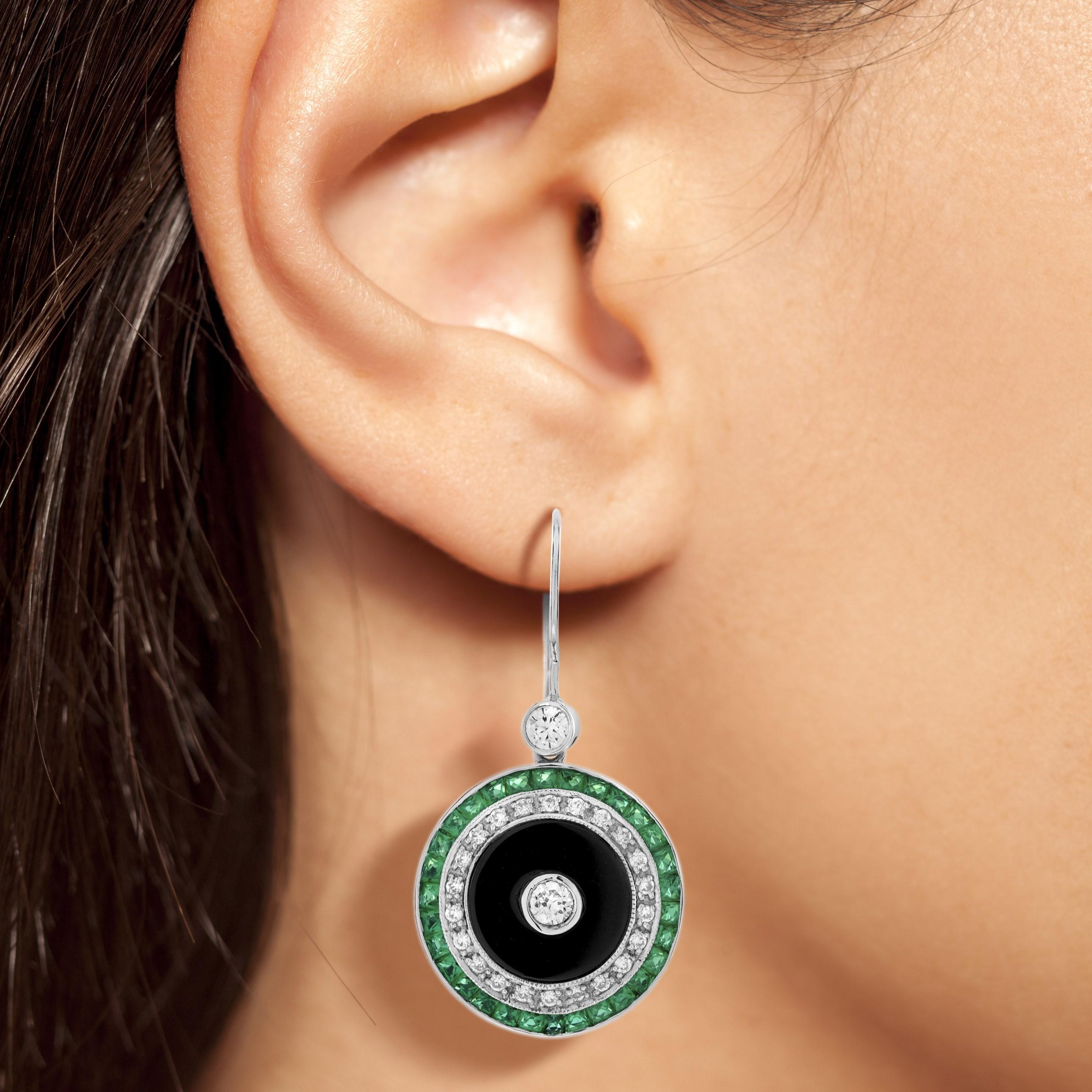 Charming Art Deco style target earrings featuring a diamond center surrounded onyx, round brilliant cut diamonds and French cut emeralds crafted in 14k white gold. Designed perfectly for a special day wear, pair them with the same design ring for