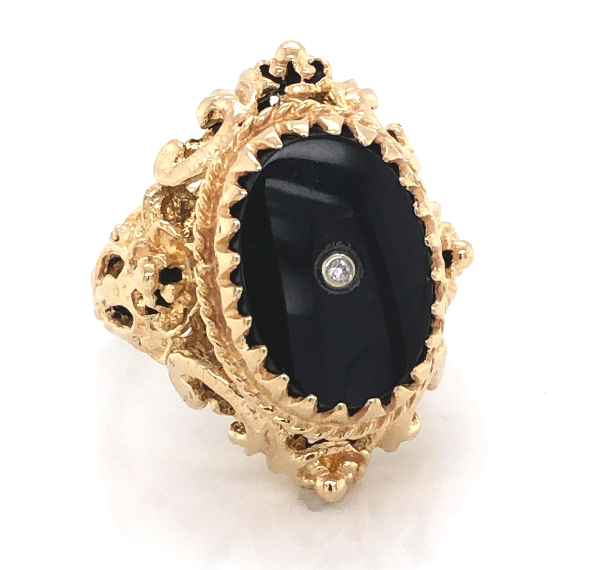 Admire this ornate Edwardian inspired ring setting created in fourteen karat 14k yellow gold that enhances the bold polished oval black onyx face with singular diamond accent. The ring measures approximately 1 inch x 5/8 inch with a depth of 3/8