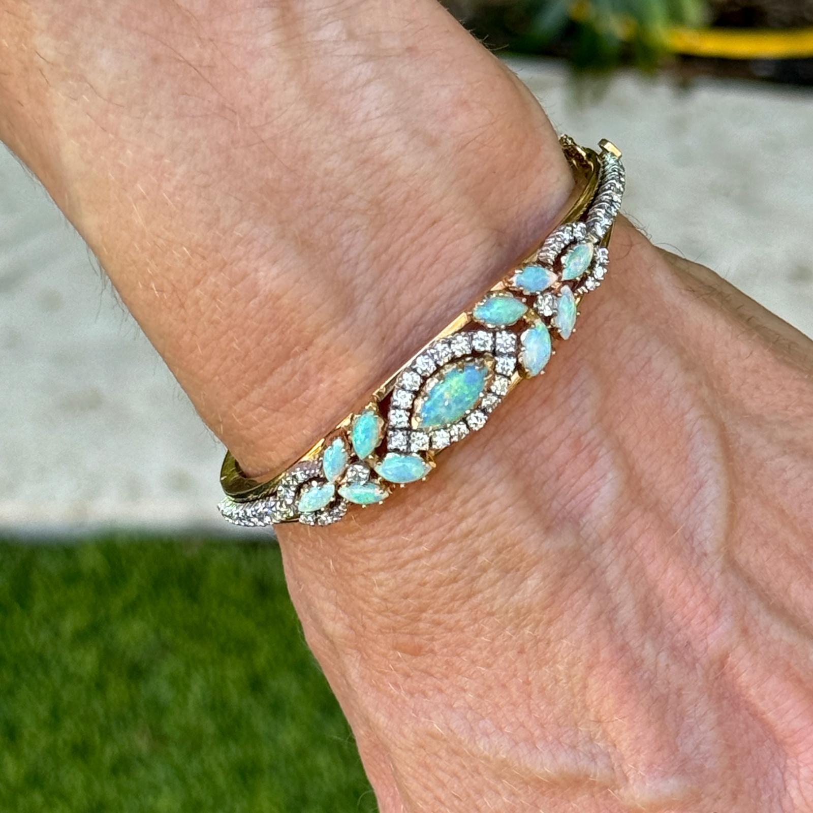 Embrace the allure of timeless elegance with this exquisite vintage bangle bracelet, crafted from rich 14 karat yellow gold. This hinged oval bangle features captivating opal gemstones, renowned for their mesmerizing play of colors and ethereal