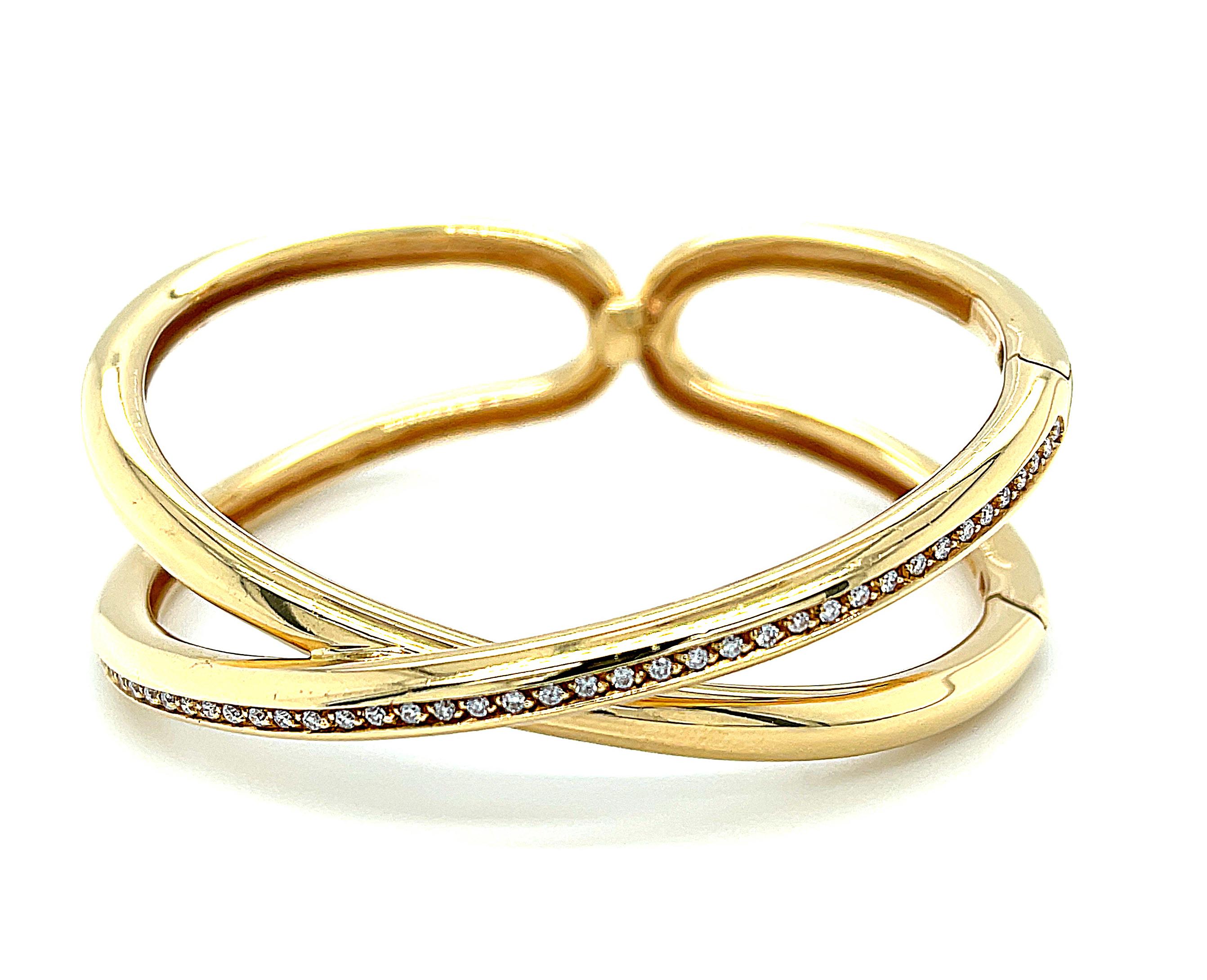 This sophisticated 18k yellow gold bangle bracelet is contemporary yet timeless, set with brilliant white diamonds in a creation by Italian jewelry designer, Antonini. Two heavy, rounded bands criss-cross to form this elegant 