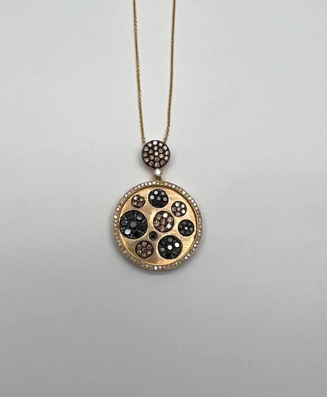 A striking pendant necklace. The pendant showcases a circular design with a mix of brown, black and white diamonds arranged in a captivating pattern. The outer edge is adorned with a border of small, sparkling diamonds, enhancing its elegance.
The
