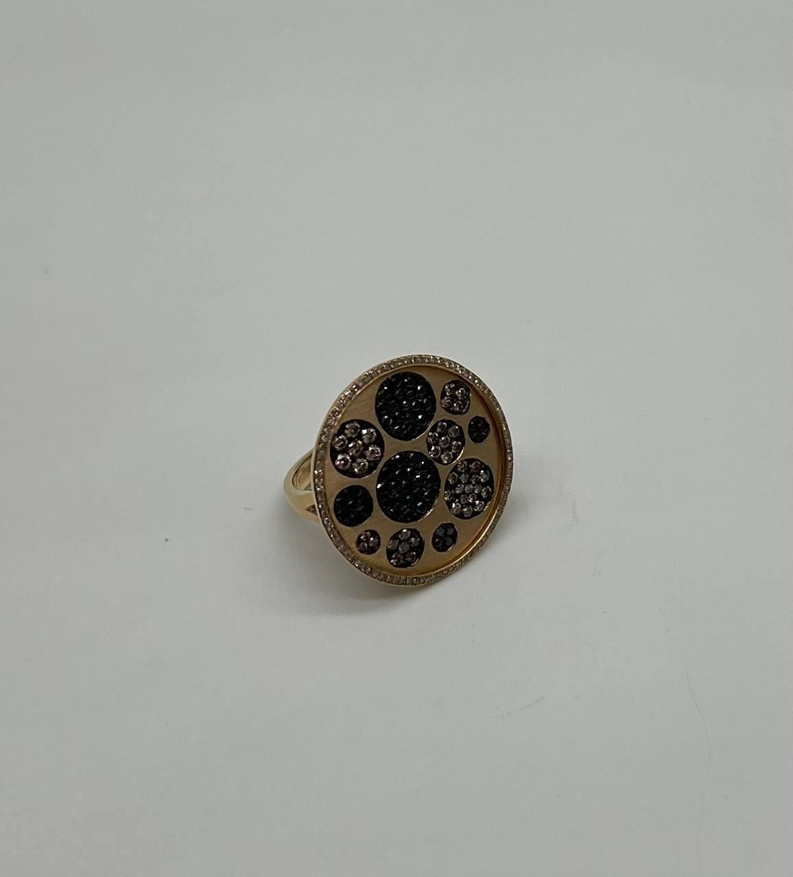 This captivating piece features a circular design with a harmonious blend of black and sparkling colored diamonds, set in a warm gold tone. The surface is adorned with an array of textured circles, creating a striking visual contrast.  The intricate