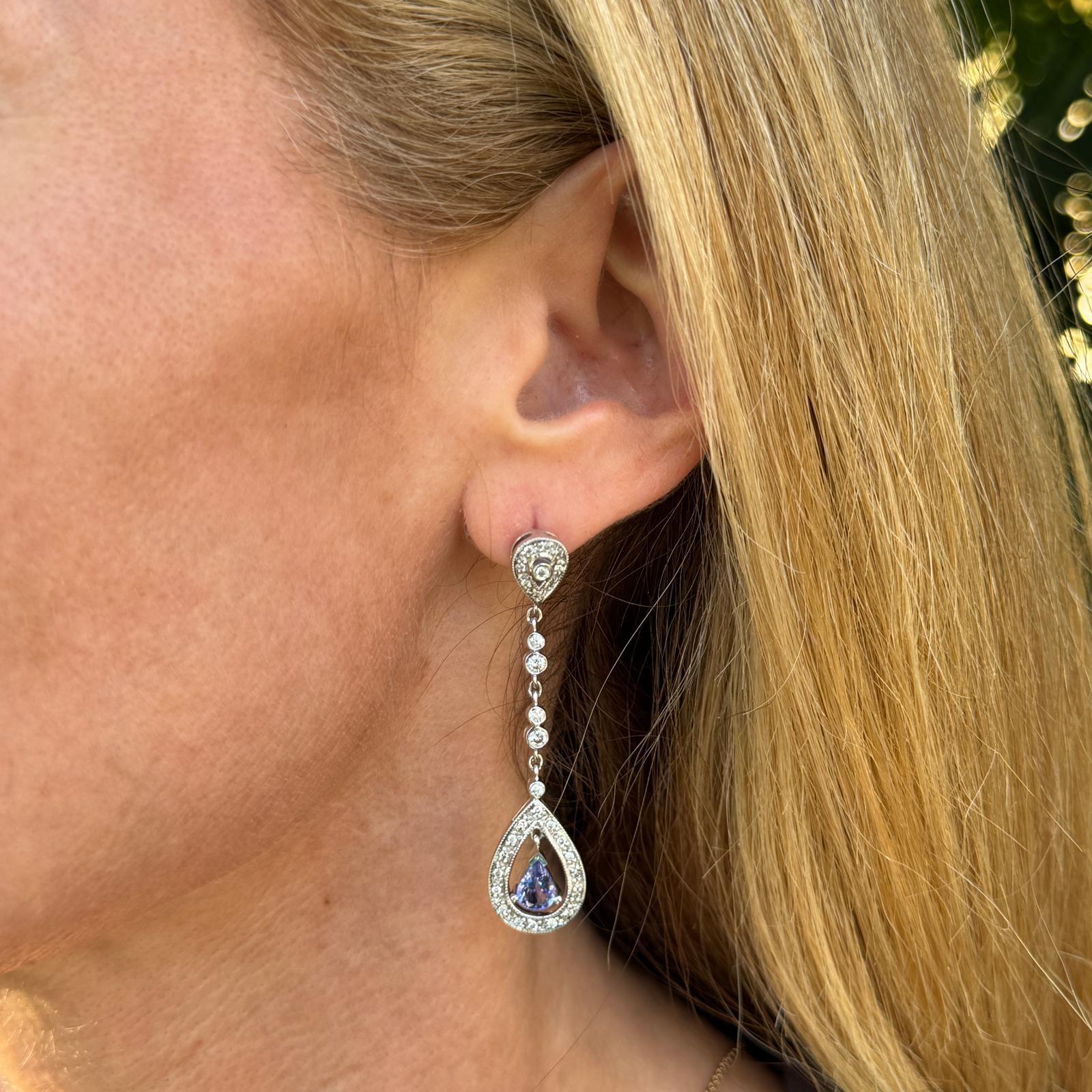 Im Mittelpunkt dieser atemberaubenden Ohrringe aus 14 Karat Weißgold stehen zwei birnenförmige Tansanite, die einen satten, leuchtenden blau-violetten Farbton aufweisen. Akzentuiert mit 60 funkelnden Diamanten mit einem Gewicht von ca. 0,50 CTW,