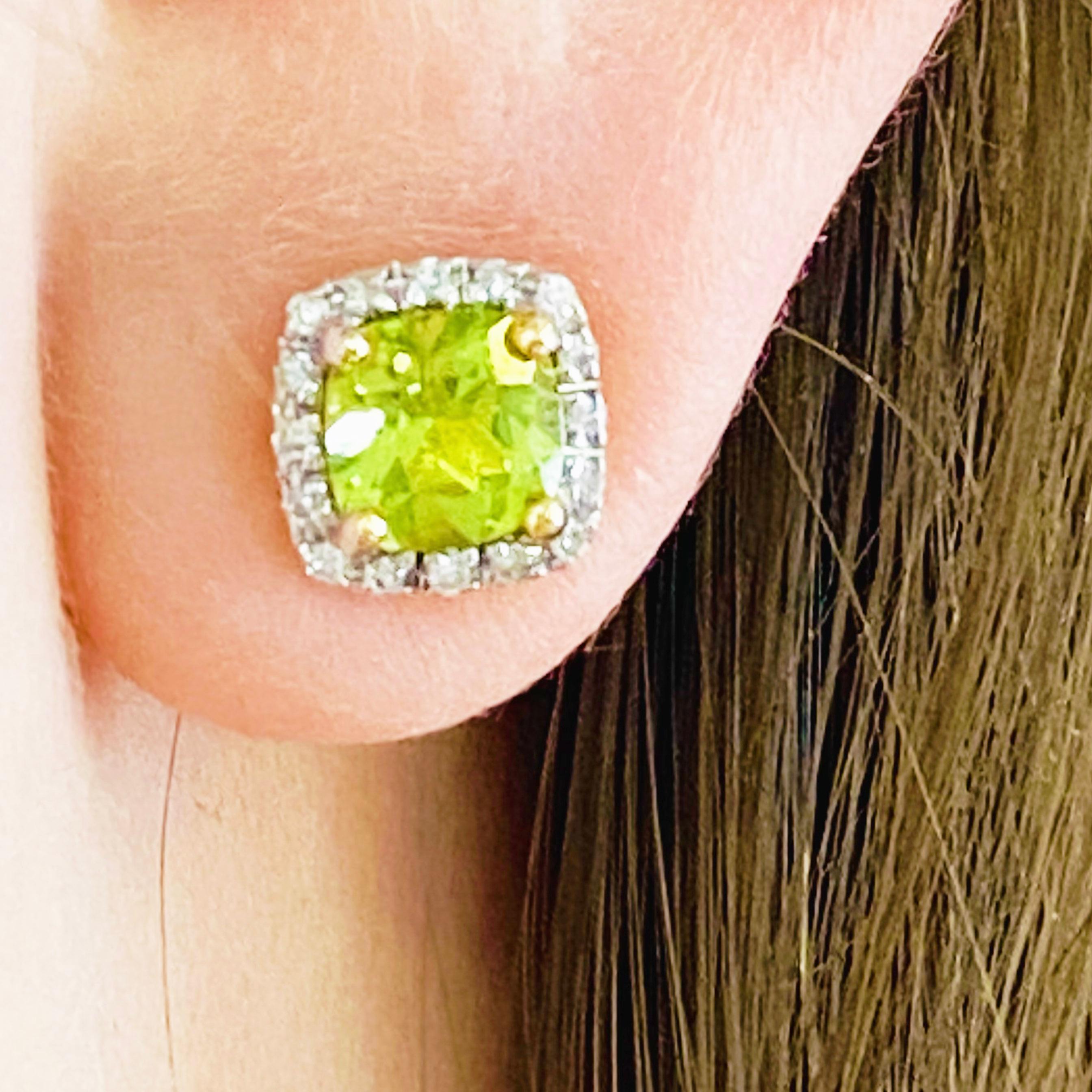 These peridot and diamond halo earrings are a modern design set in 14 karat yellow gold! Each earring holds a round, genuine peridot gemstone set in four yellow gold prongs. This bright green peridot is framed with bright white, round brilliant