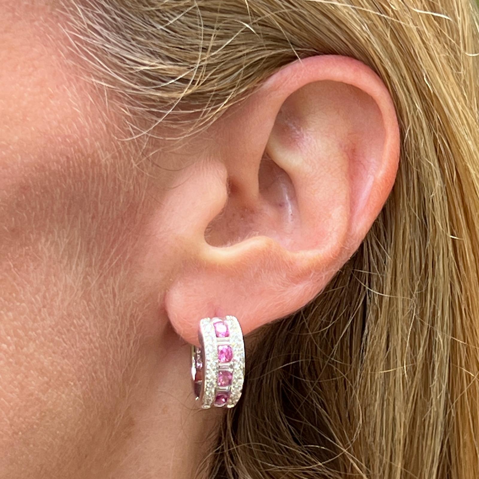 Pink sapphire diamond modern hoop earrings crafted in 18 karat white gold. The hoops feature 8 round pink sapphire gemstones separated by round brilliant and baguette cut diamonds weighing approximately 1.00 carat total weight. The diamonds are
