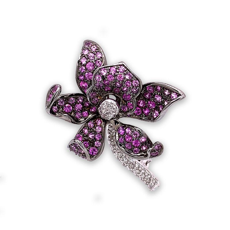 A glowing pink orchid with a life-like design. It features 1.50 carats of pink sapphire in various shades to made up the orchid lips. The stem and piston on the flower are set with round cut diamonds, 0.50 carats, and they are set in 18k white gold