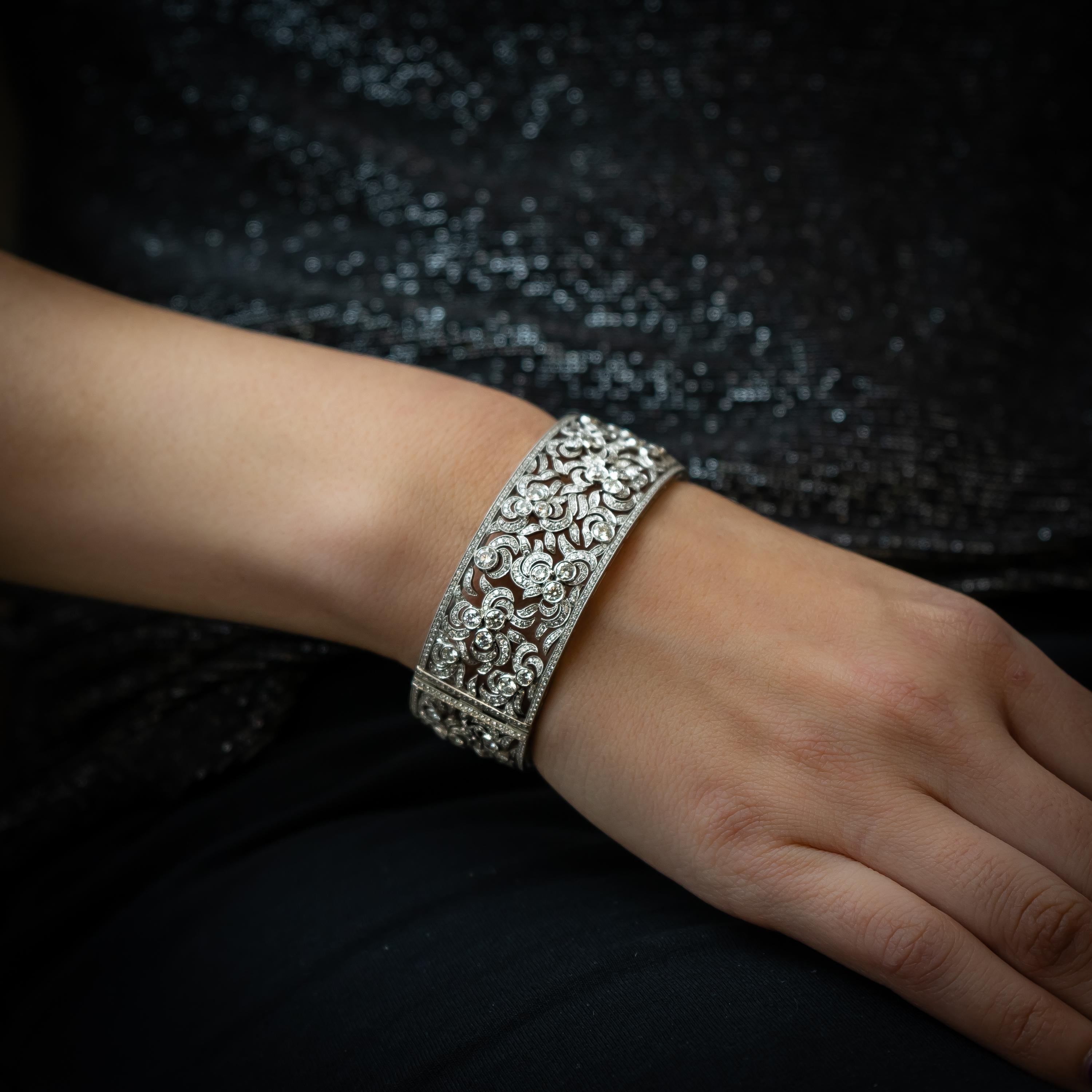 A modern diamond clasp bangle, set with 11.23ct of round brilliant-cut diamonds, in rub over and pavé settings, with millegrain edges, with an openwork swirl design, mounted in platinum. 