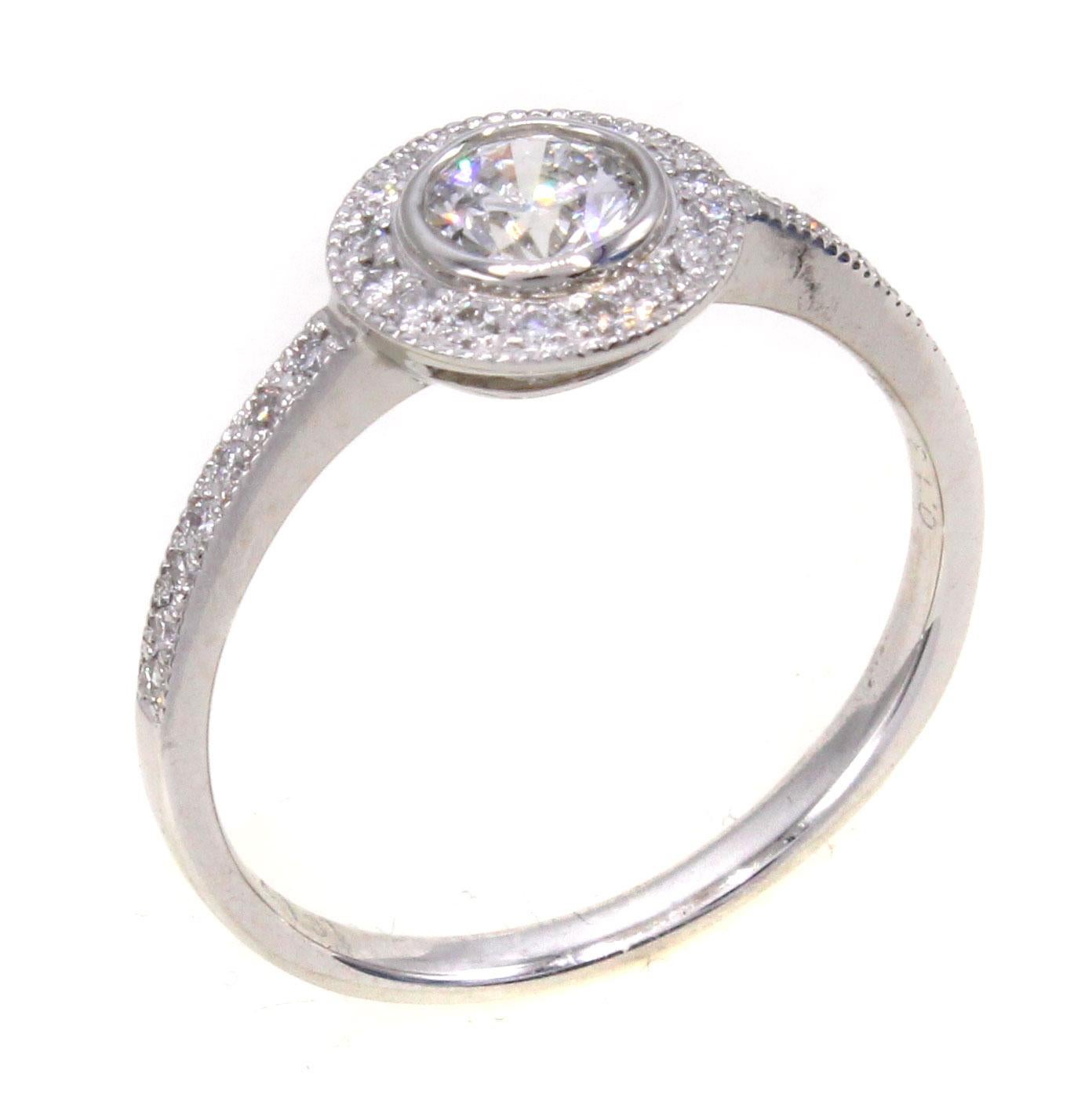 Beautifully designed and masterfully handcrafted in platinum, this perfect engagement ring features a centrally bezel set round brilliant cut diamond weighing 0.41 carats. Surrounding this diamond is a halo of bright white round brilliant cut