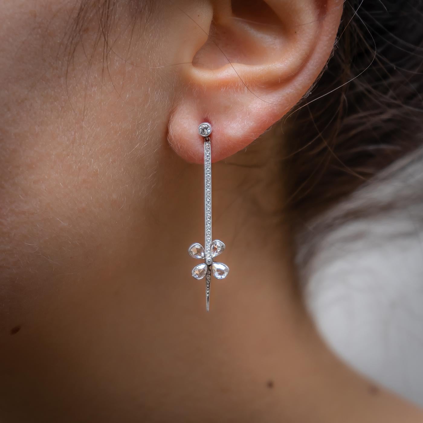 A pair of diamond flower drop earrings, with a rose-cut diamond set flower at the bottom, in millegrain edged settings, with diamond set tops and a pavé set bar between. With post and butterfly fittings.
