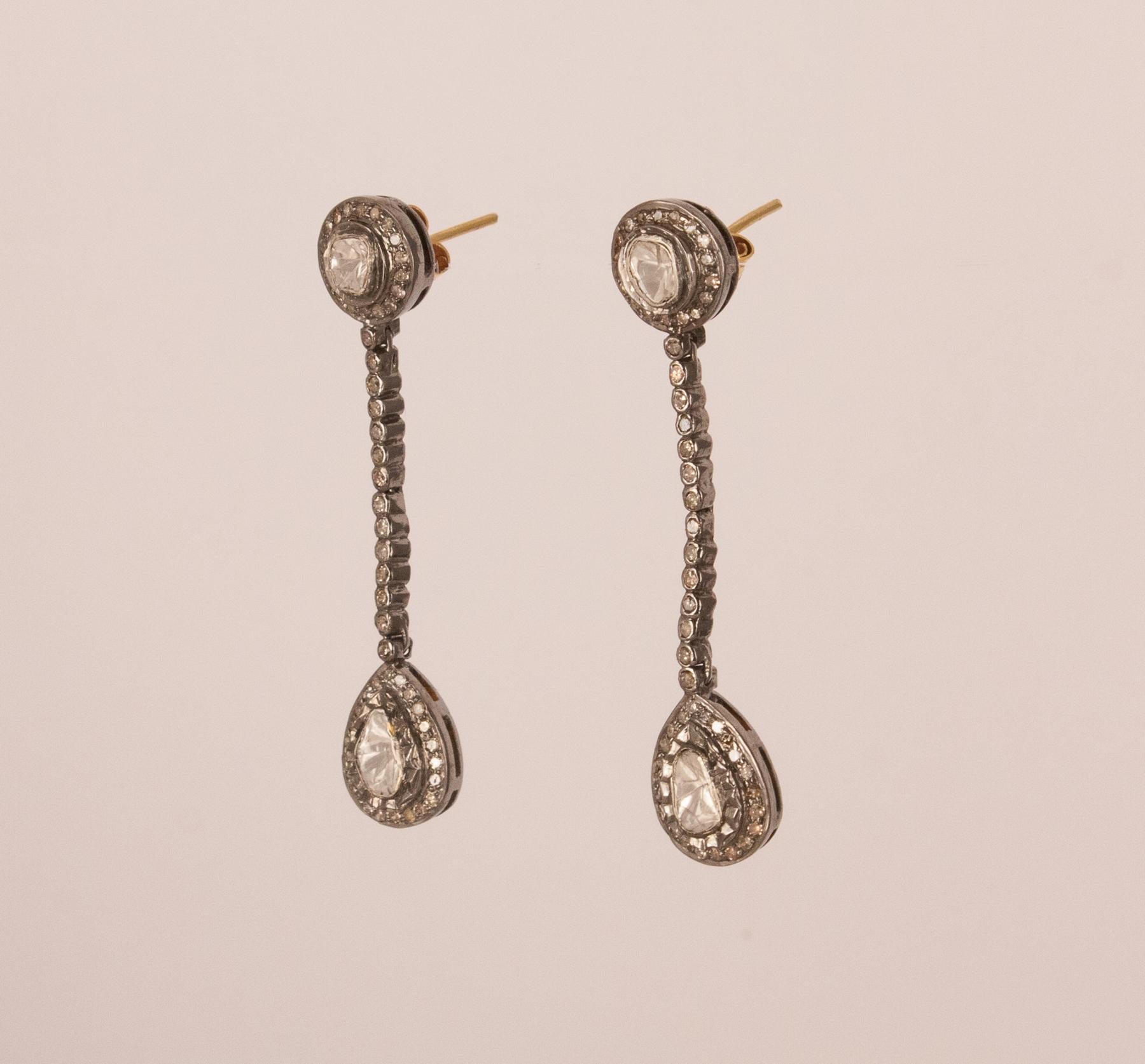 These rose cut diamond dangle earrings feature larger, asymmetrical Polki diamonds encircled by diamonds pave set in sterling silver and joined by a strand of smaller diamonds. Set in this traditional Indian style, the earrings are at once elegant