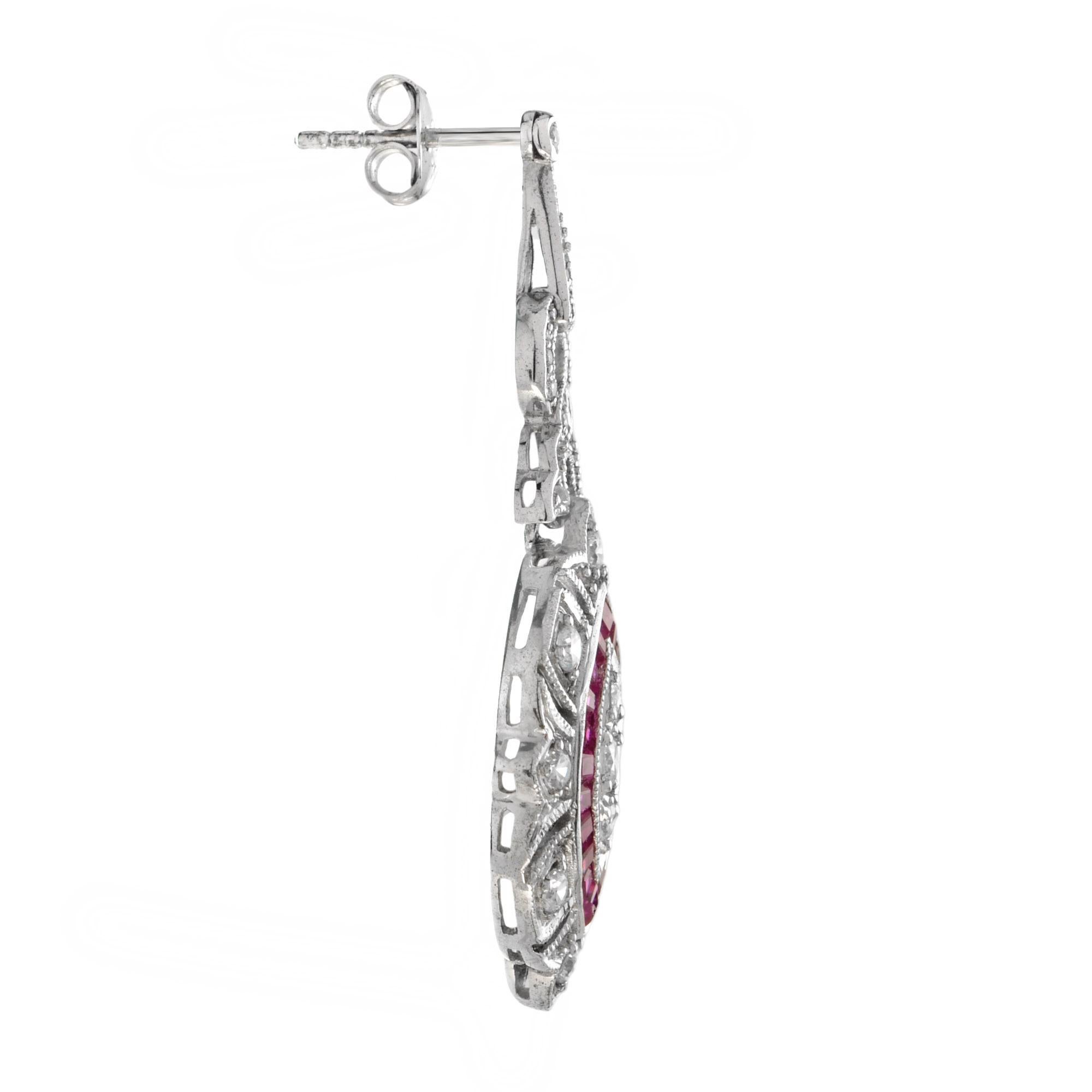 These beautiful Art Deco style dangle earrings are finished in brightly polished. Delicately set across the face of the earrings are three round diamonds surrounded by French cut natural ruby. The entire earring is adorned with round diamonds. Truly