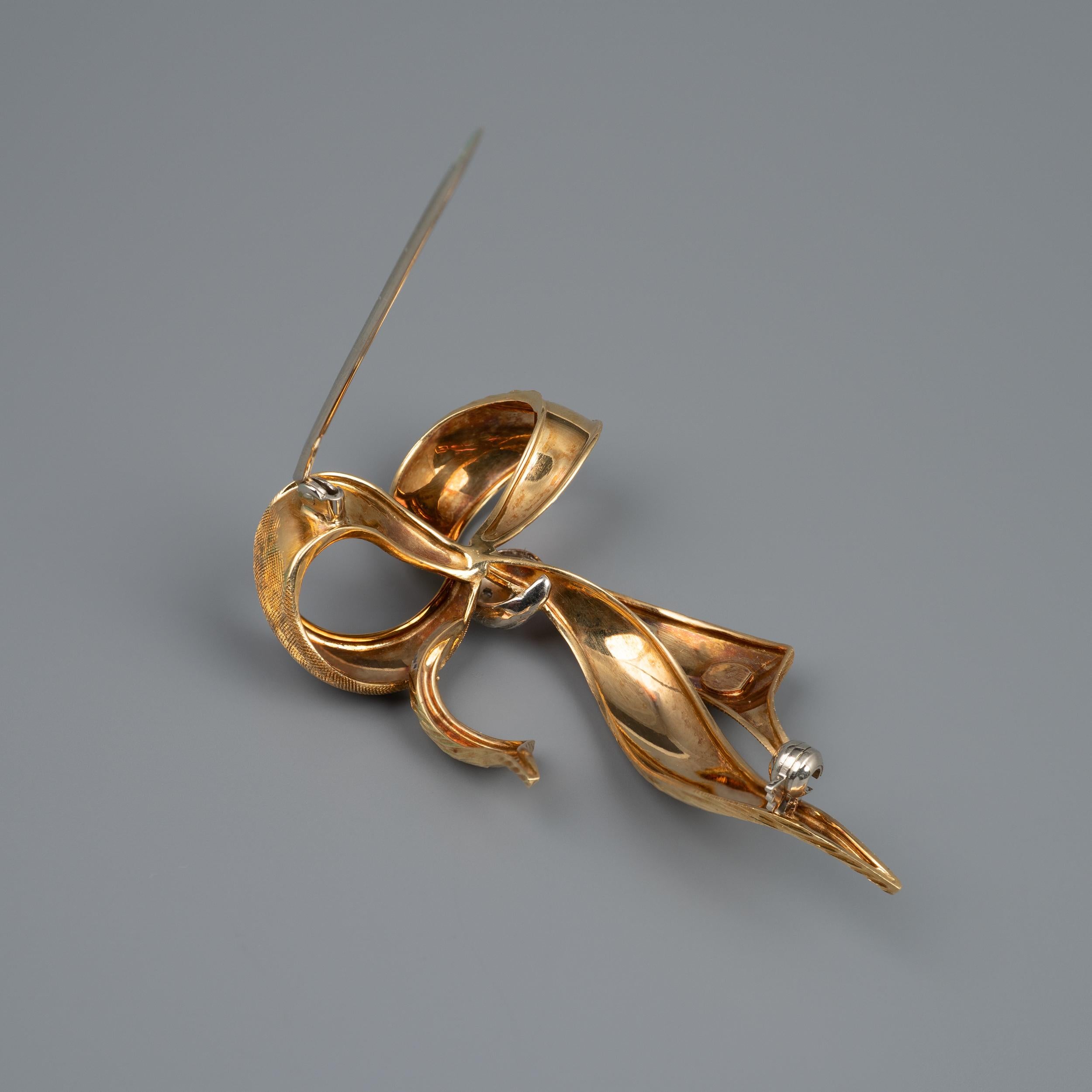 This 18 karat gold vintage Ribbon Bow brooch features diamonds set in white gold.

A substantial size, the brooch is crafted into loops of gold ribbon crafted with two different textures. The center of the bow has a white gold band set with three