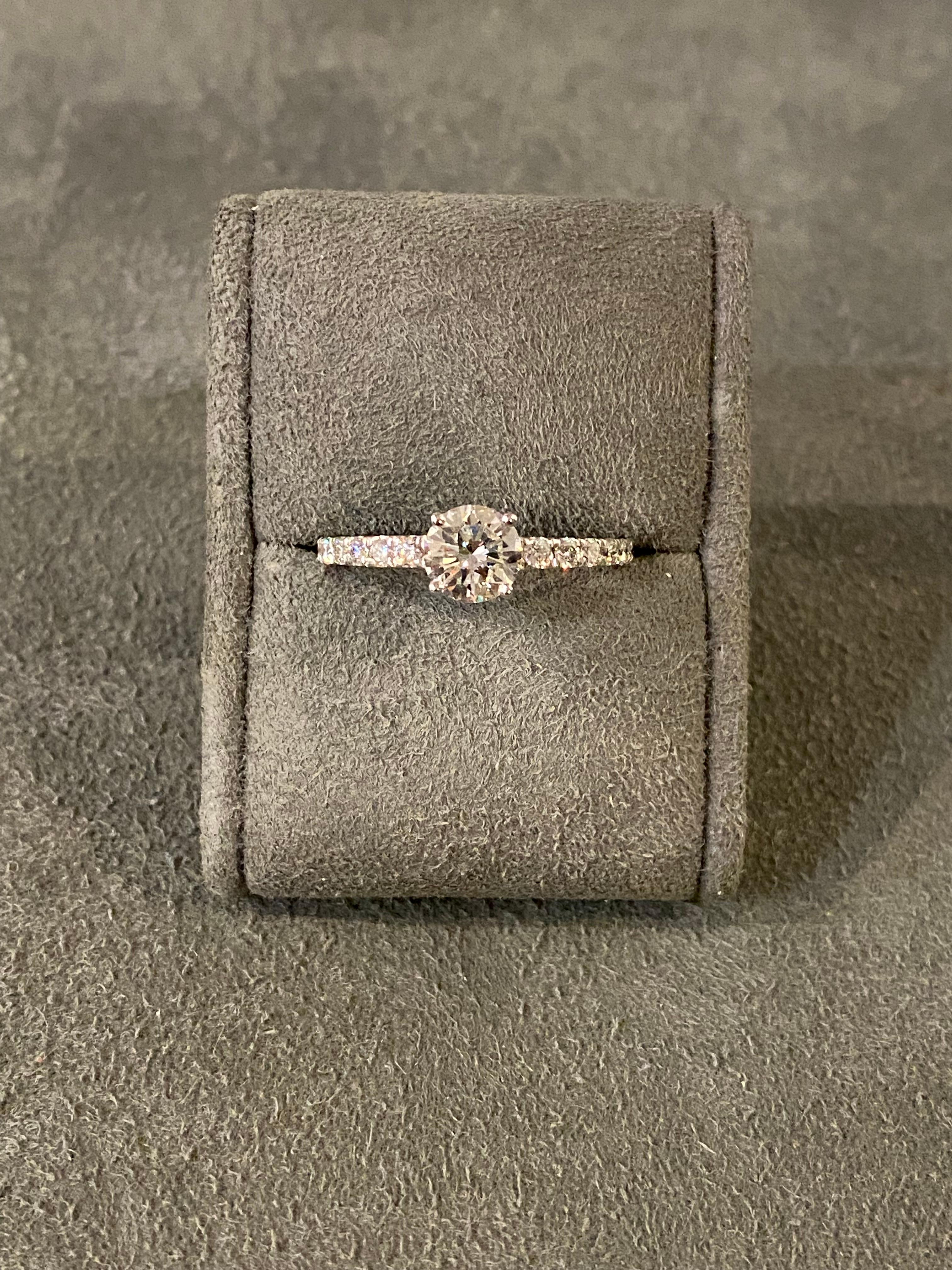 Un diamante (aproximadamente 0,85 ct, 6 mm) engastado con 14 diamantes más pequeños (aproximadamente 0,28 ct) en oro blanco de 18k. La piedra central es de calidad G VS (no certificada). Talla EU 52. 