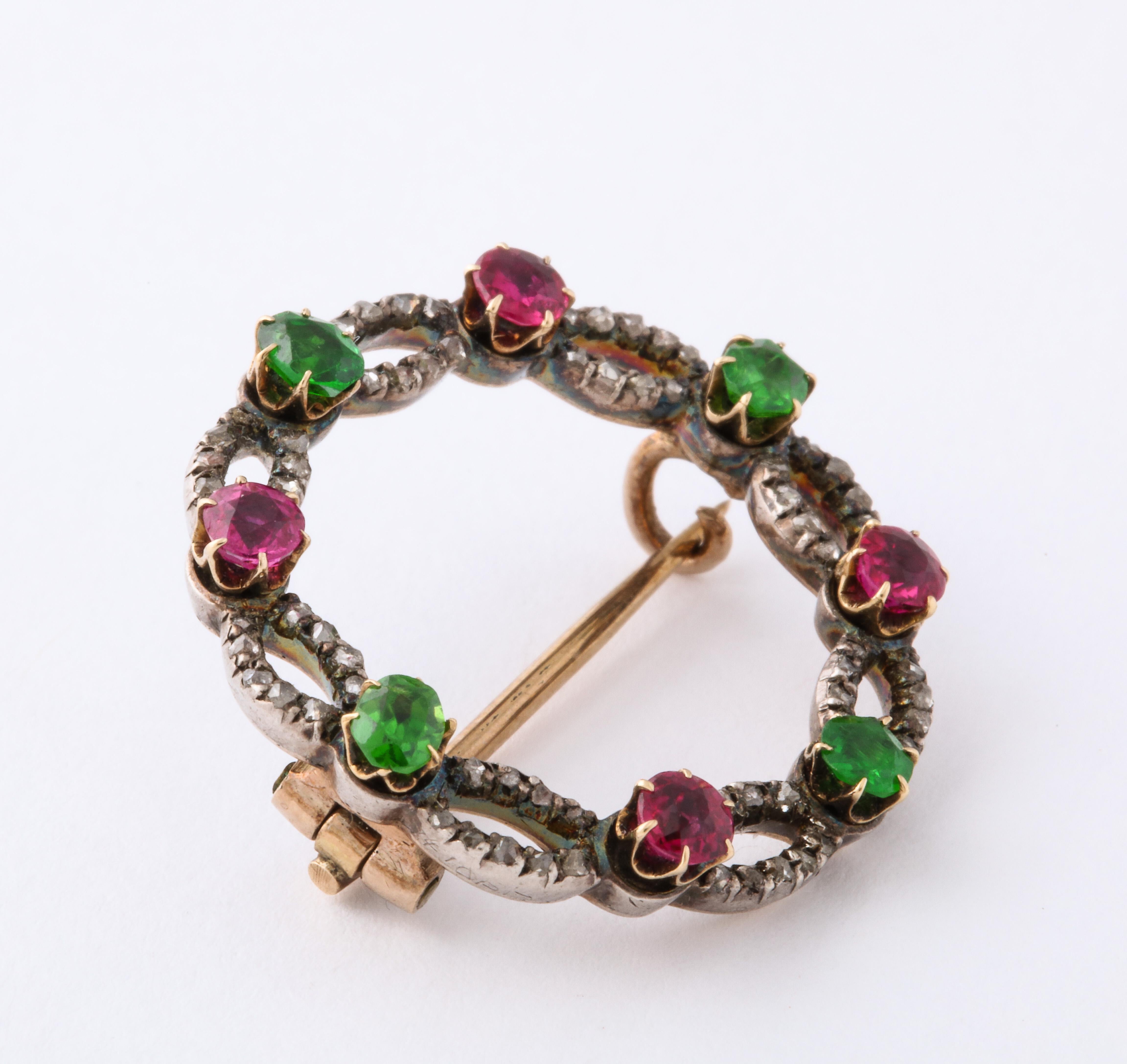Lovely little circular brooch with sections of rose cut diamonds divided by alternating rubies and demantoid garnets. Silver on yellow gold. Just under 1