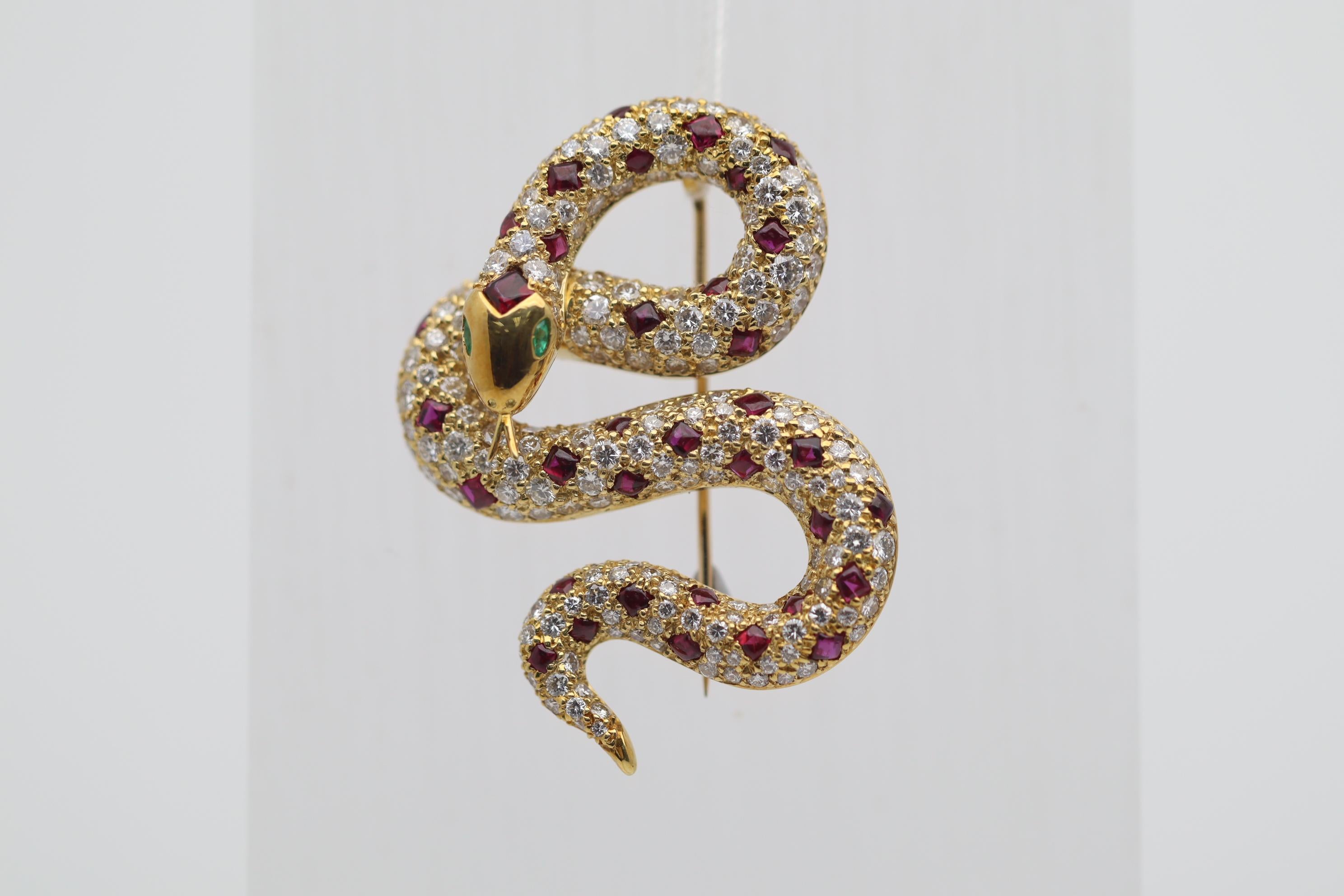 A chic and elegant brooch depicting a coiled gem-studded snake! It features 3.22 carats of round brilliant-cut diamonds which are bright white and clean. Adding to that are 2.64 carats of square shaped cabochon rubies creating a pattern on the