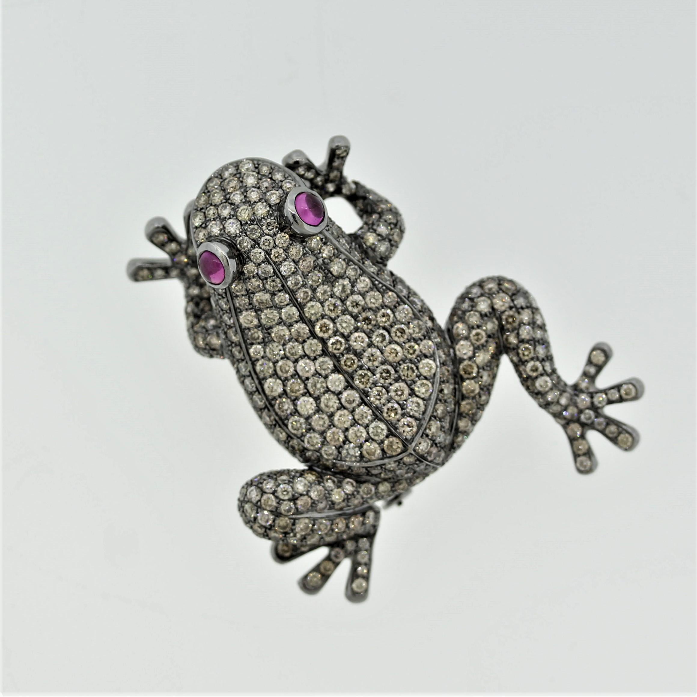 A diamond studded gold frog hopping about! It features 6.22 carats of round brilliant-cut diamonds with a soft and subtle fancy chocolaty color. It has 2 ruby cabochons as its eyes. The piece is made in 18k gold with a rhodium finish giving the frog