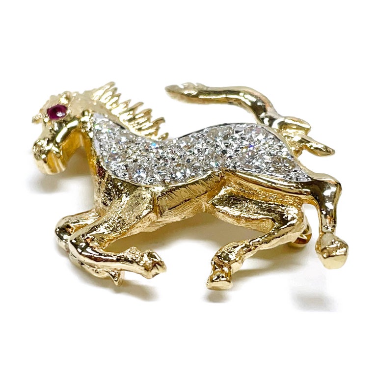 18 Karat Yellow Gold Diamond Ruby Horse Brooch/Pin. The brooch features twelve 2mm round diamonds for a total carat weight of 0.24ctw. The brooch measures 23.8mm tall x 30mm wide. There is a single round Ruby flush set in the eye. The brooch has