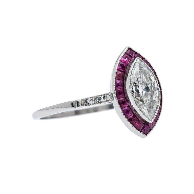 Featuring a 0.91 carat marquise cut diamond that is approximately  I-J color, SI2 clarity. Surrounded  by a halo of calibrated rubies individually cut to perfectly fit and compliment the center diamond. Hand crafted in platinum. Ring size 7-1/4 and
