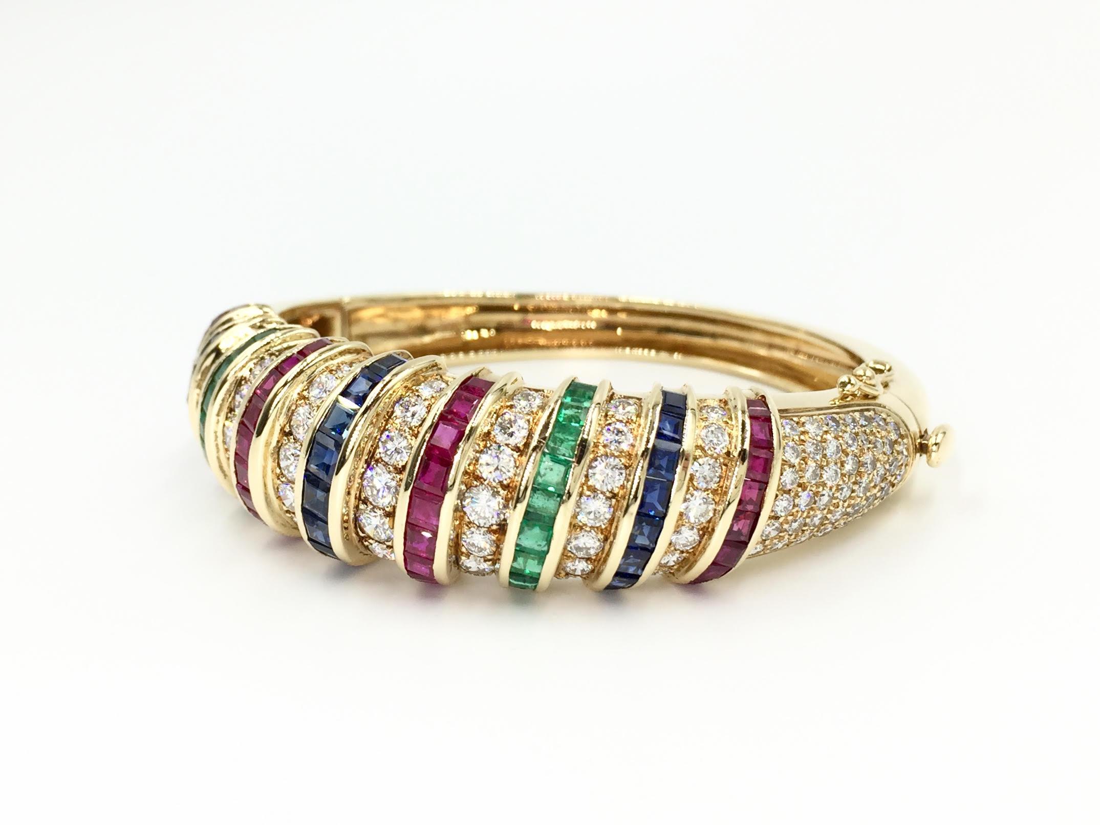 A beautiful 18 karat yellow gold bangle bracelet featuring high quality diamonds (approximately F color, VS2-SI1) rich royal blue sapphires, vibrant rubies and vivid emeralds. Precious colored stones are all of very fine quality and expertly set in