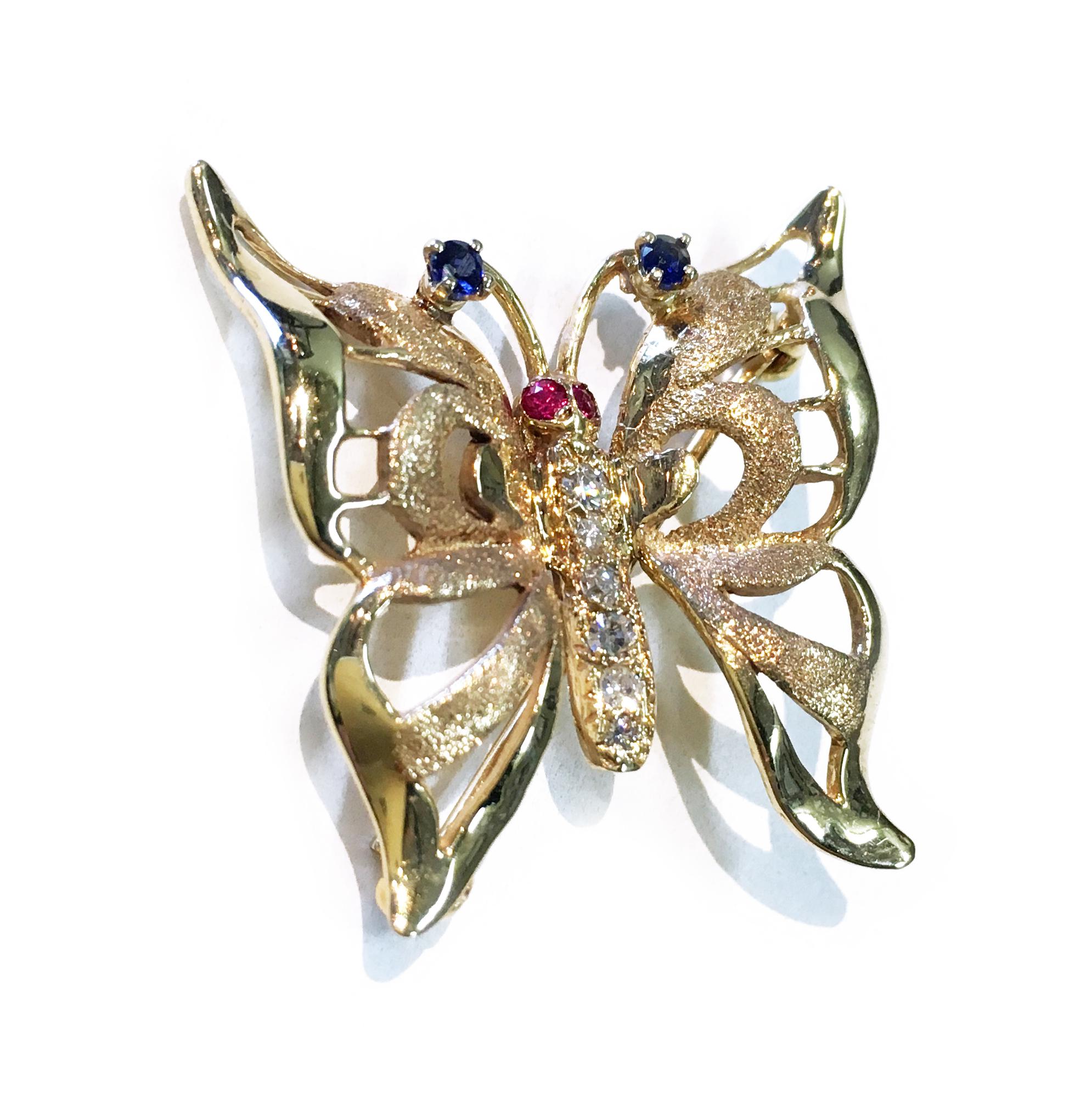 Diamond Ruby Sapphire Butterfly Brooch/Pin. Six round diamonds are bead-set on the body, two round Rubies set in the eyes, and two blue Sapphires prong-set at the tip of the antennae. The diamonds have a total carat weight of 0.20ctw. This lovely