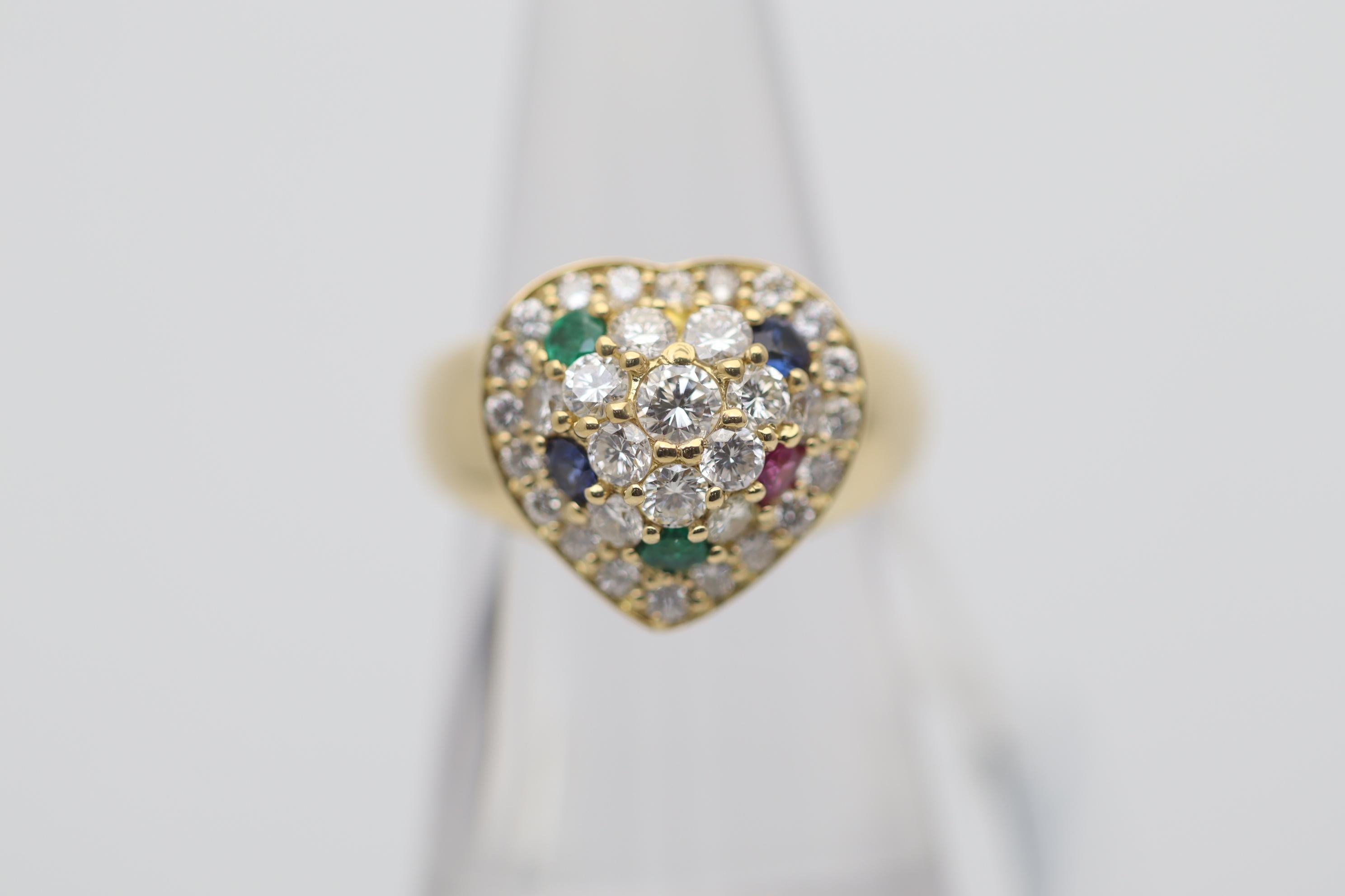 A sweet and stylish ring featuring a gold heart motif studded with diamonds and gems. The heart is studded with 1.14 carats of round brilliant-cut diamonds along with two emeralds, two sapphires, and one ruby, which add color and contrast. Made in