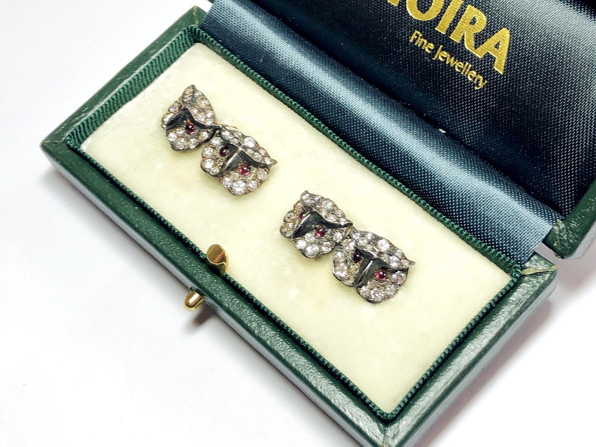 A pair of owl cufflinks, pavé set with a mixture of old and brilliant cut diamonds, with cabochon ruby set eyes, with chain links, mounted in silver-upon-gold, circa 1970. Each head of the owl measures approximately 10mm x 13mm.