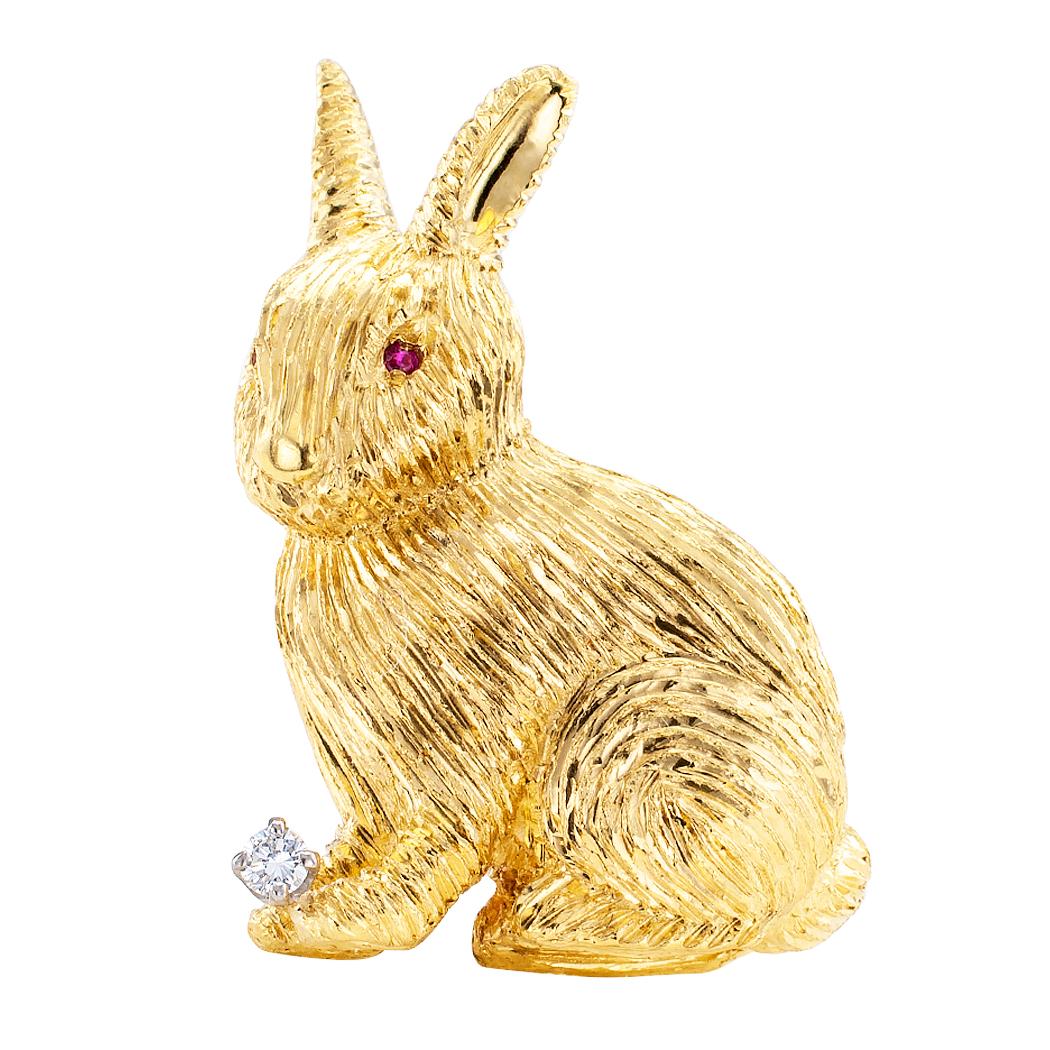 Diamond ruby and gold bunny rabbit brooch circa 1970. The figural design depicts a bunny rabbit with ruby-set eyes, cuddling a round brilliant-cut diamond between its front paws. The diamond weighing approximately 0.05 carat, approximately G color