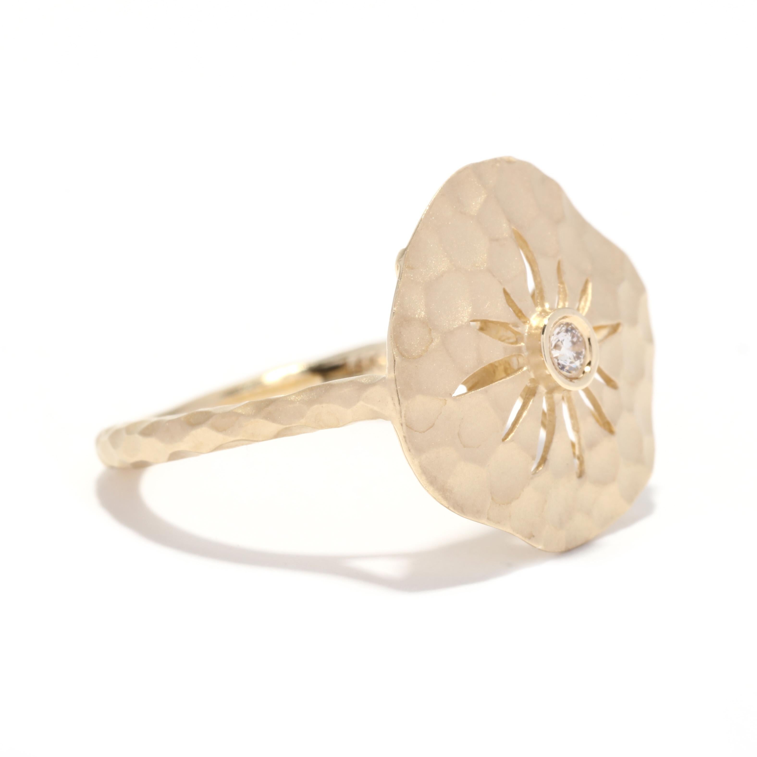 A 14 karat yellow gold diamond sand dollar ring by Gabriel. This ring feats a matte, hammered sand dollar motif with a bezel set, full cut round diamond in the center weighing .03 carat and a thin hammered band.

Stones:
- diamond, 1 stone
- full