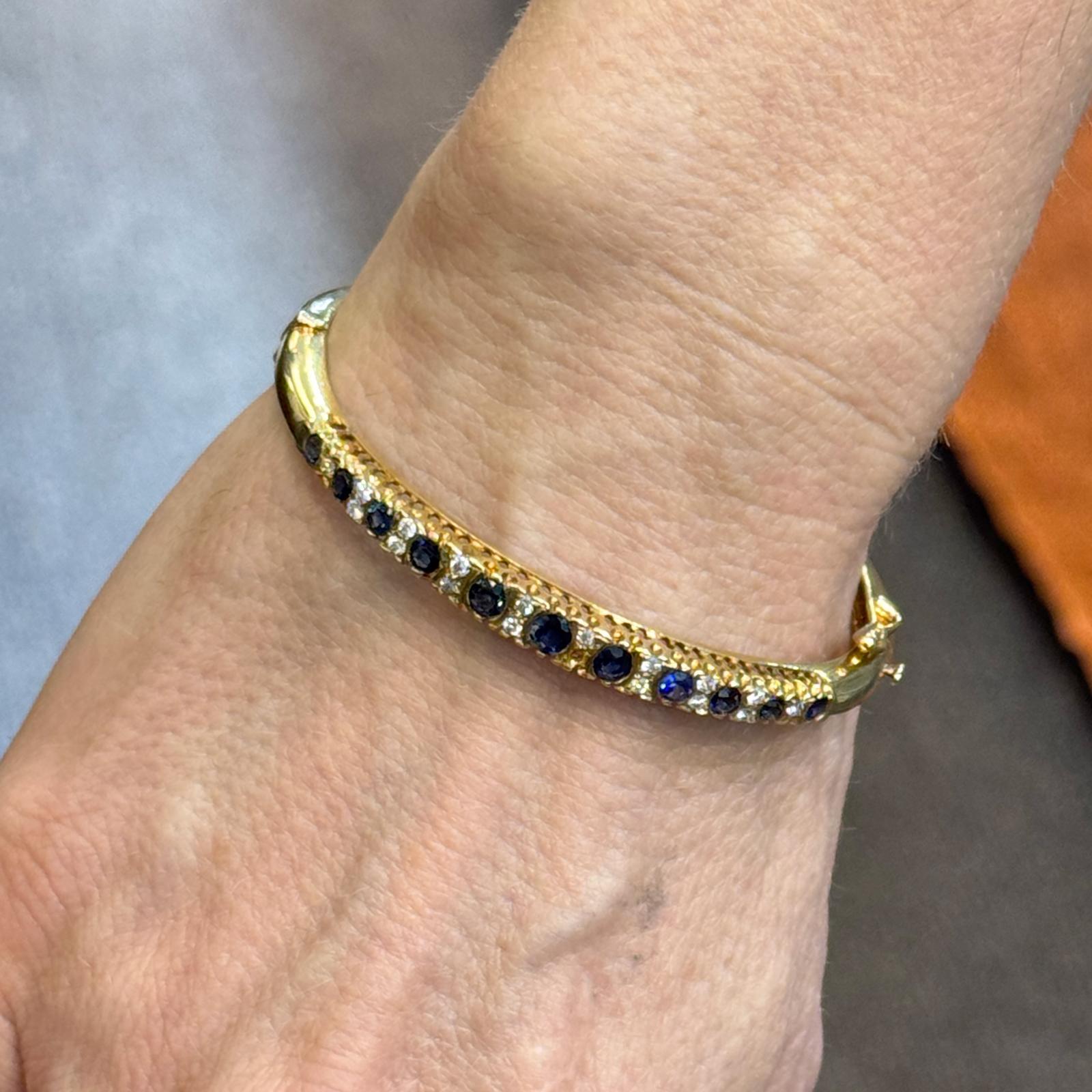Dieser elegante Armreif aus 14 Karat Gelbgold besticht durch eine raffinierte Kombination aus Diamanten und Saphiren. Das Armband ist mit 18 runden Diamanten im Brillantschliff von insgesamt 0,36 Karat mit der Farbe G-H und der Reinheit VS2-SI1