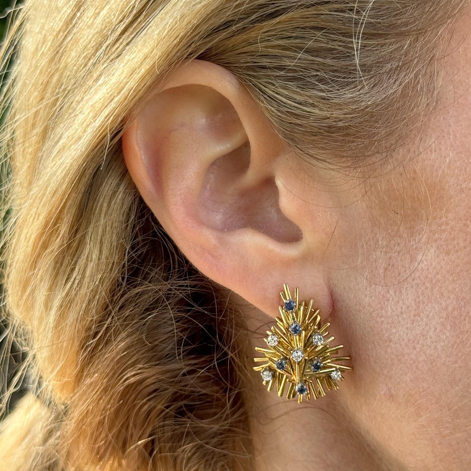 The diamond and sapphire earrings feature a spray design, typical of the 1960's vintage style. Fashioned in 18 karat yellow gold, these earrings boast a rich and luxurious metal setting that perfectly complements the diamonds and sapphires.  The