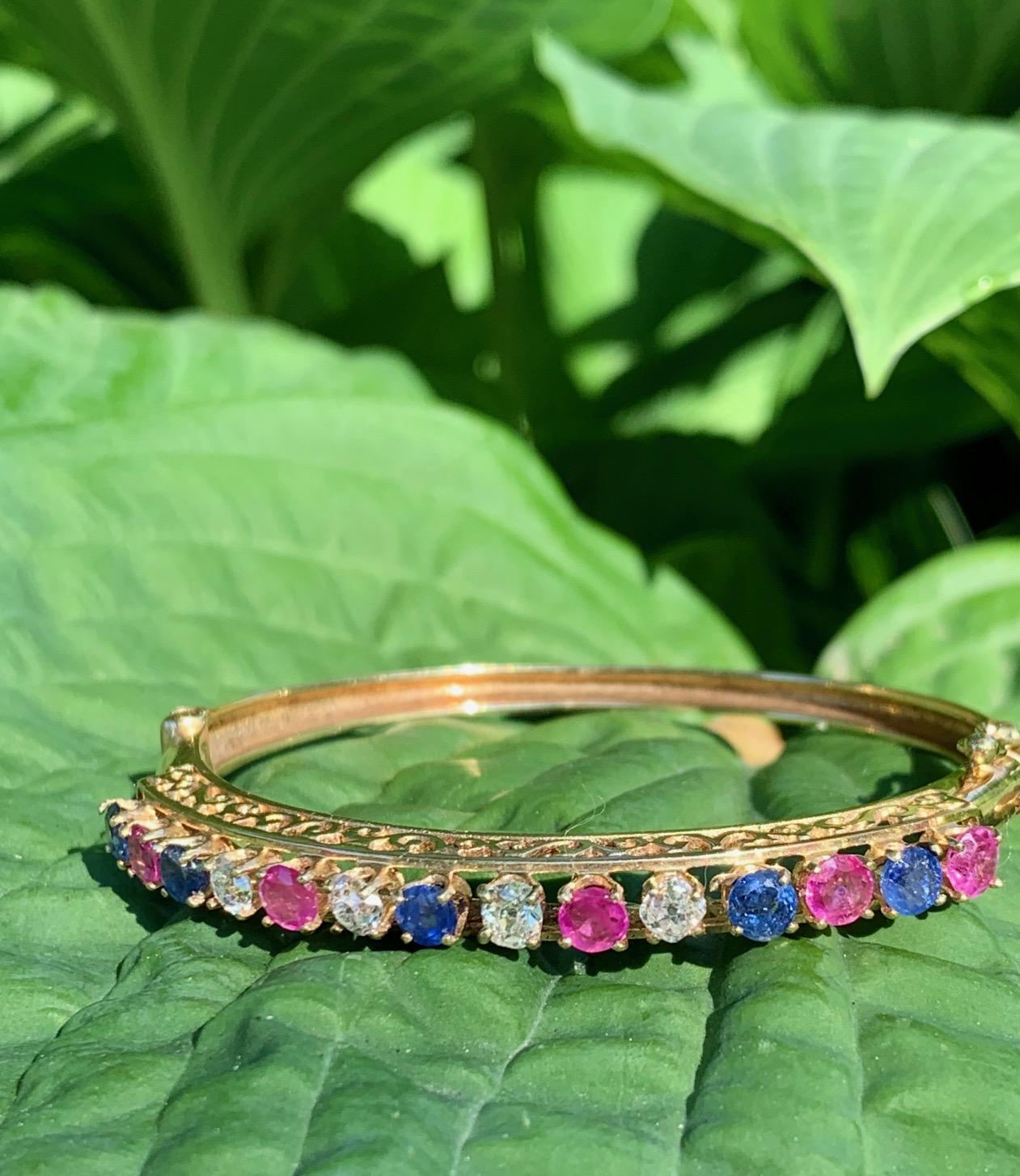 This beautiful modern (1970's) 14k yellow gold bangle features round cut diamonds, rubies and sapphires.  A latch opening closes with a box clasp and a safety hook.
It is stamped 14k.

There are four round cut diamonds; five pink/red rubies; and