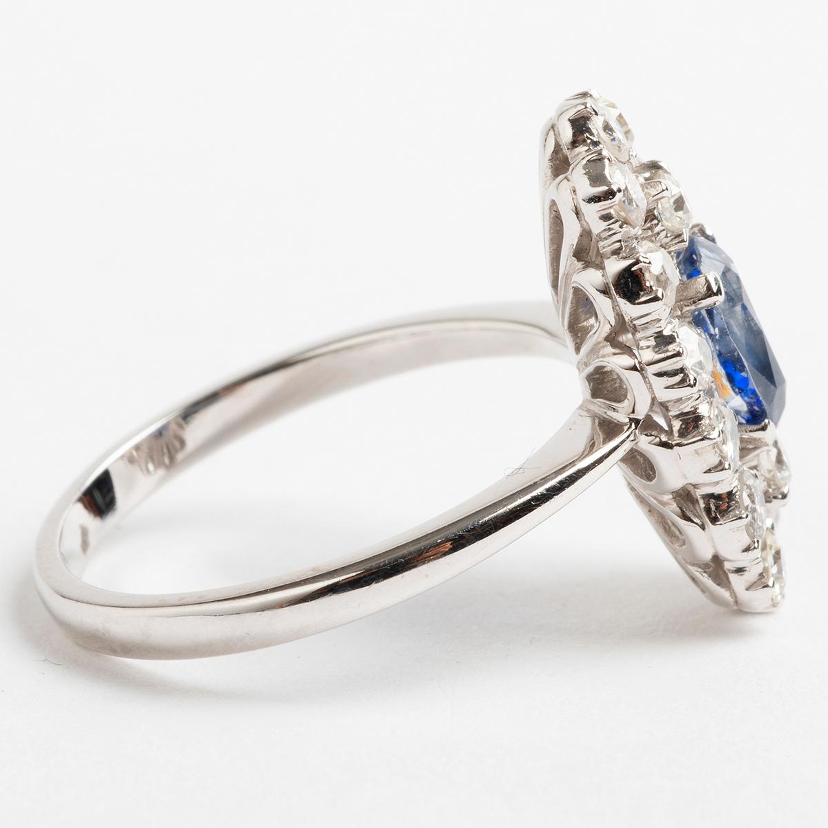 A large sapphire cluster ring, of 18k white gold. The oval cut Sapphire is set in a four claw setting surrounded by sixteen round cut diamonds totalling est. 1.12carat. A prominent and elegant piece, the ring size is P. The stones cover 2cm x 1cm