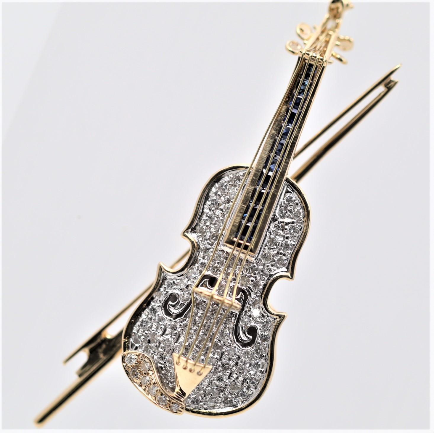 A precious violin made in 18k yellow gold! It features 0.74 carats of round brilliant-cut diamonds along with a row of square-shape blue sapphire under the strings weighing 0.55 carats. The back of the brooch is hand-polished and textured to appear